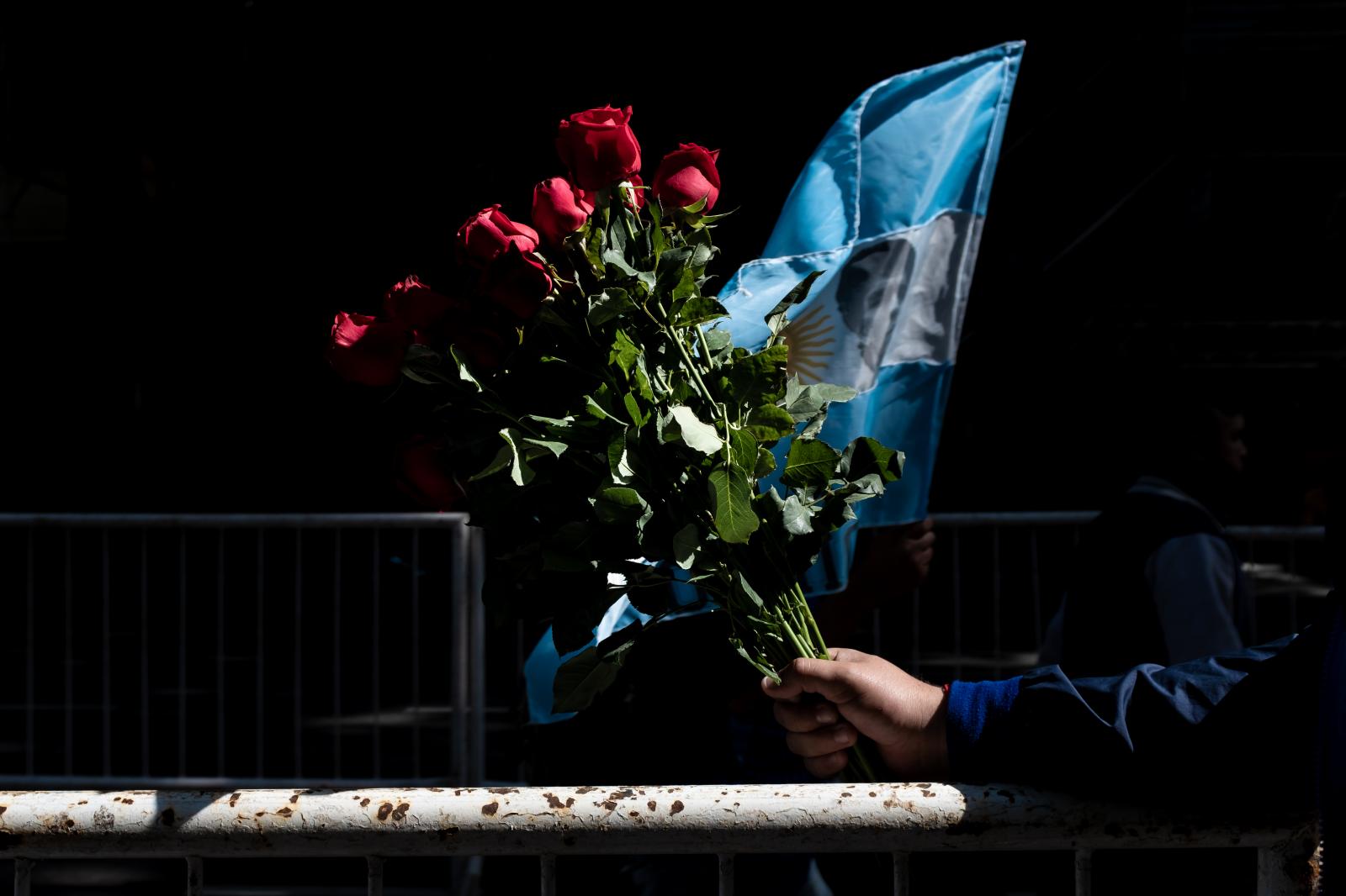 A street vendor holds out a bou...nirs and flowers to their idol.