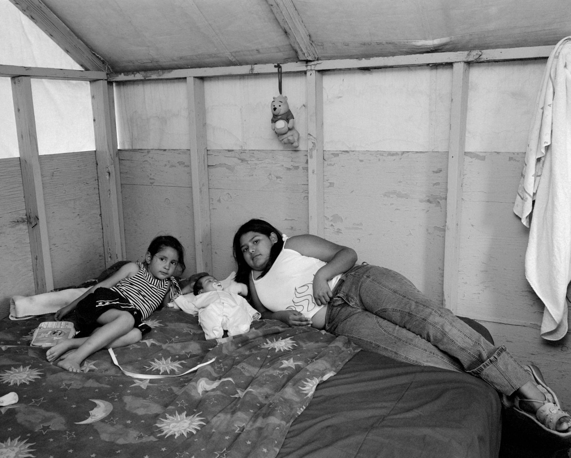 Estela (on the right), her younger sister, and their one month old cousin Amy in the cabin of their aunt in a migrant farmworker camp at a cherry farm. Estela&rsquo;s family originates from Mexico, lives in California now, but annually follows the harvest from the Pacific southwest to the northwest, picking cherries, apples and pears. The children were born in the United States and are American citizens. The Dalles, Oregon, USA. July 2005. From the photo story The Farmworkers&#39; Children. 