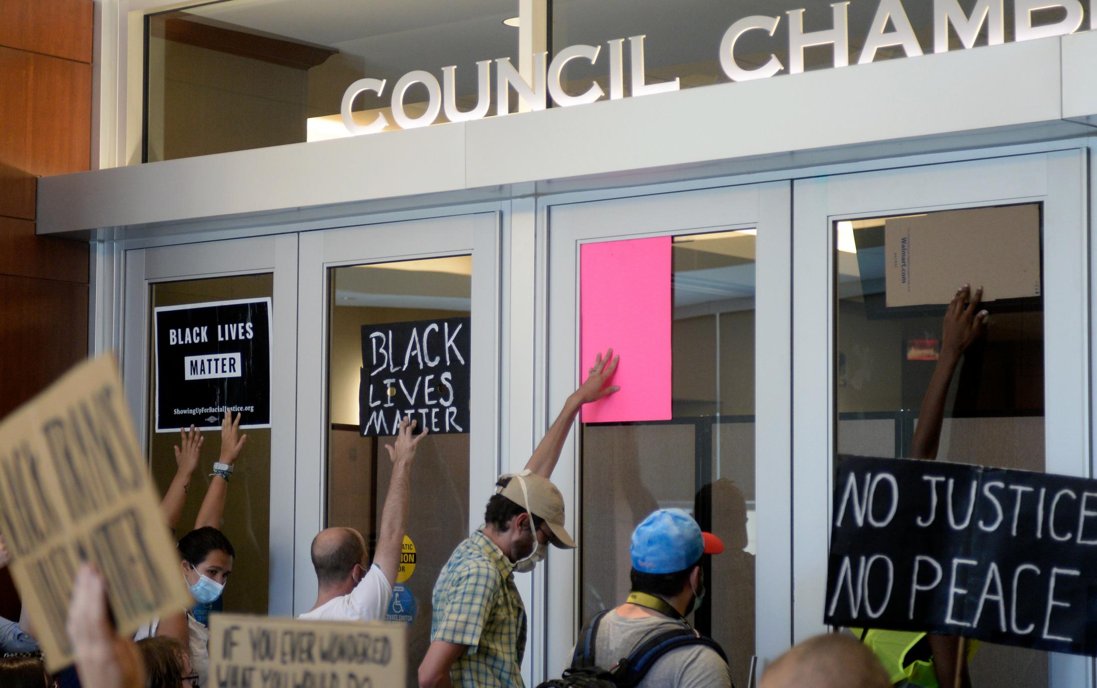 A Summer of Social Justice - Protesters hold up signs in front of the Council Chamber...