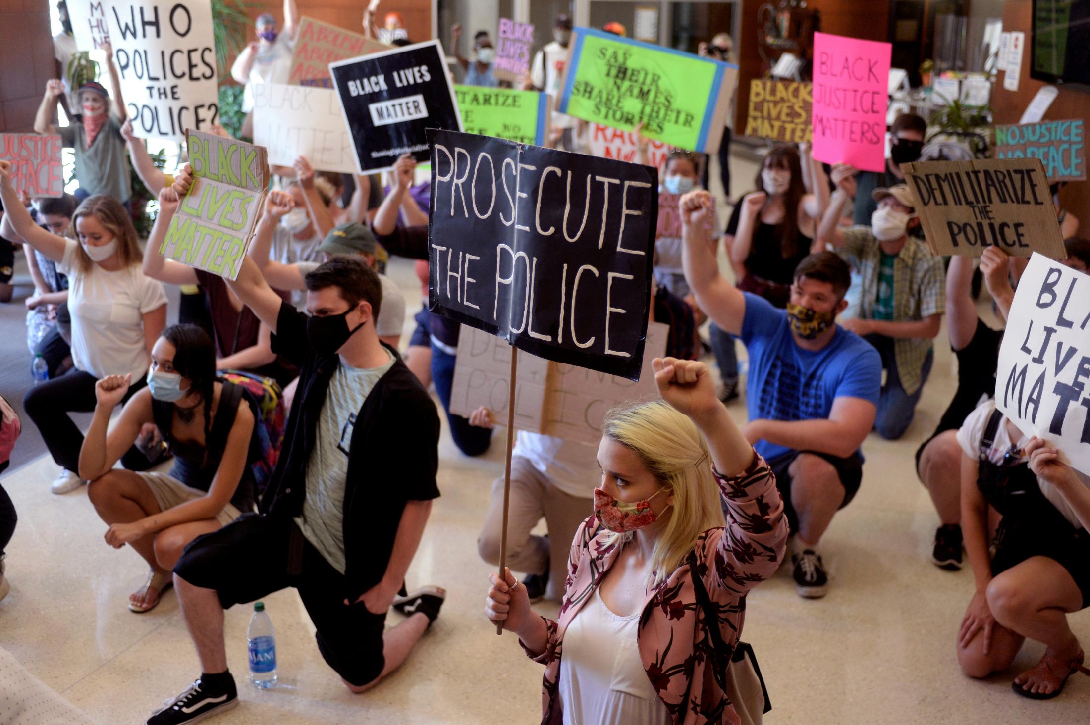 A Summer of Social Justice - Rally attendees kneel while holding up protest signs on...