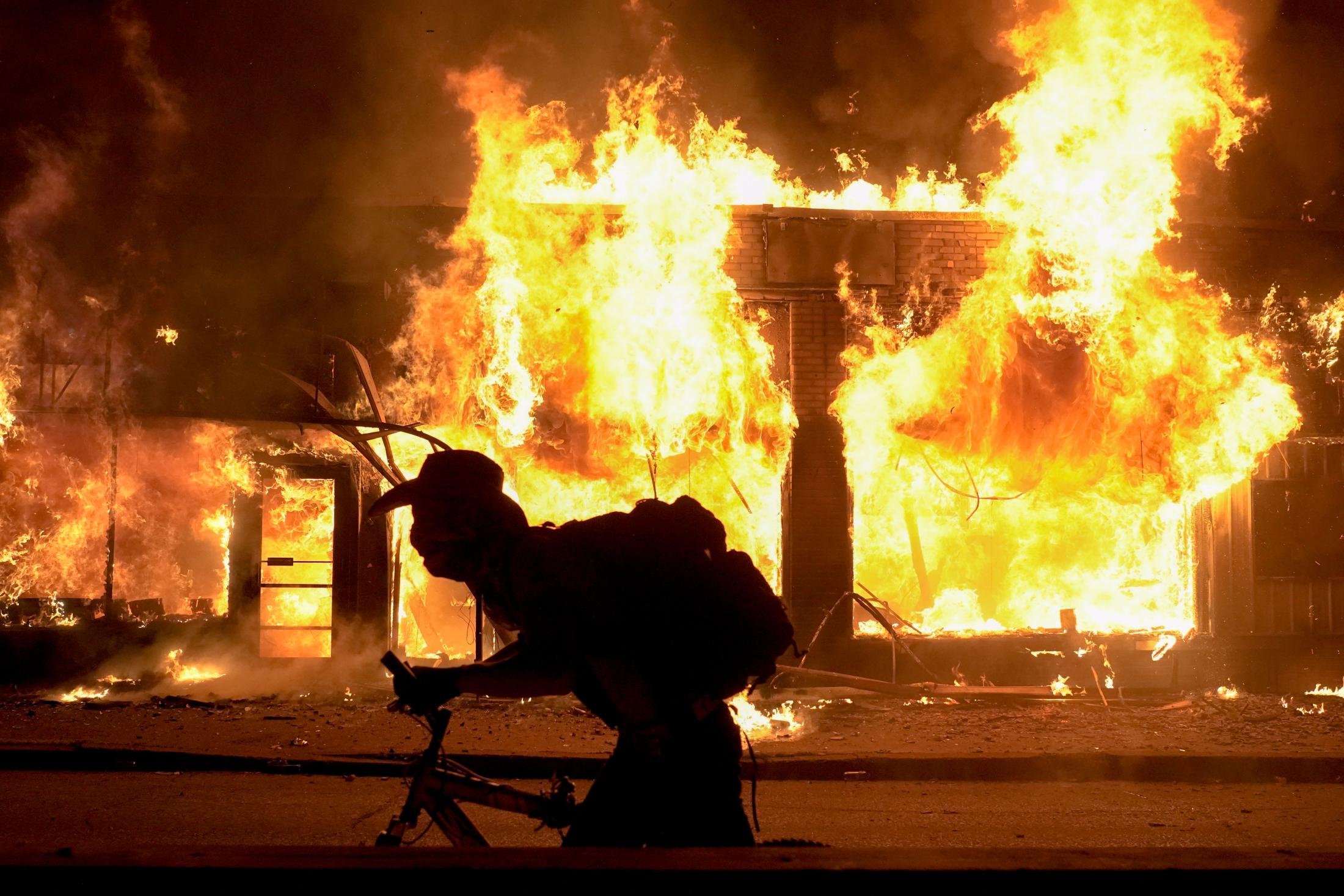The BLM Summer - A biker rides past a burning building on Friday, May 29,...