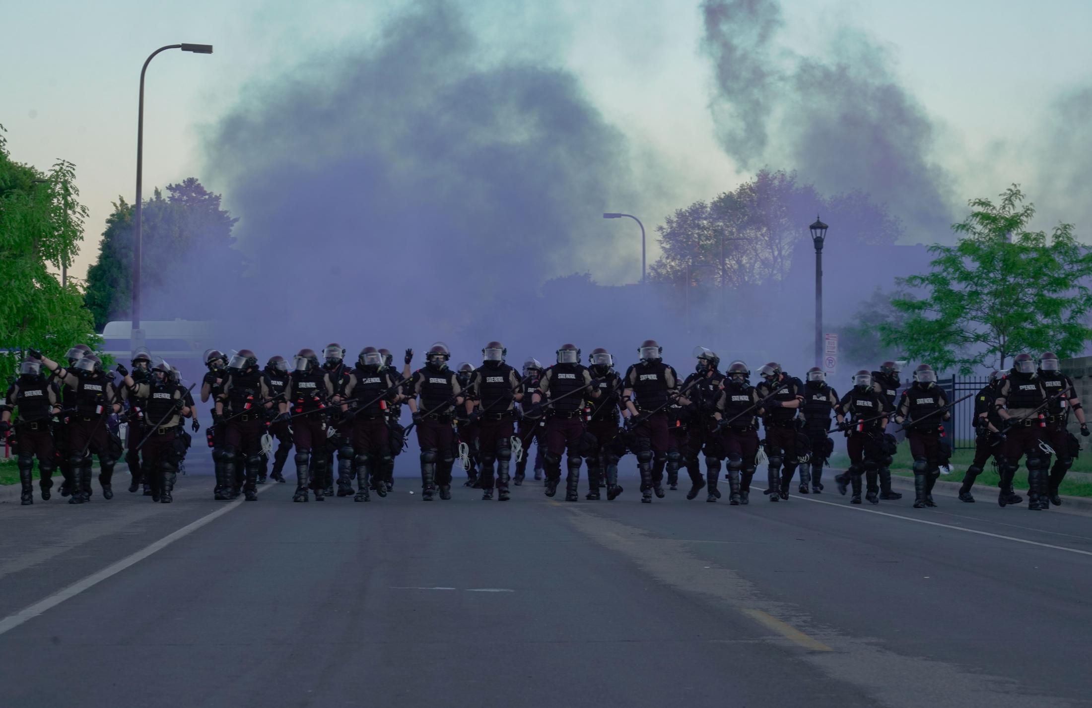 The BLM Summer - Minneapolis riot police walk through a cloud of purple...