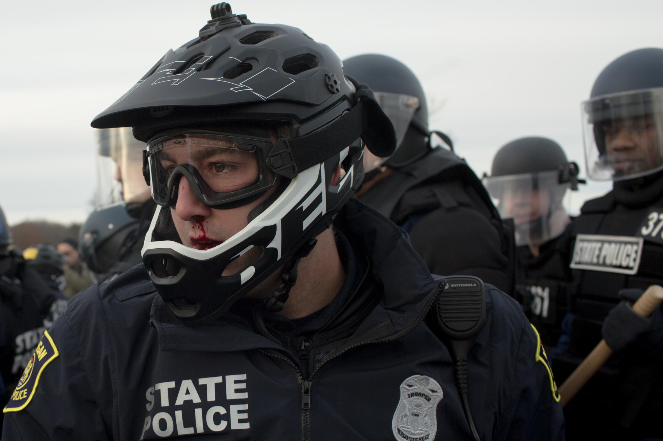 Portraits - A Michigan State Police Officer with a bloody nose uses...