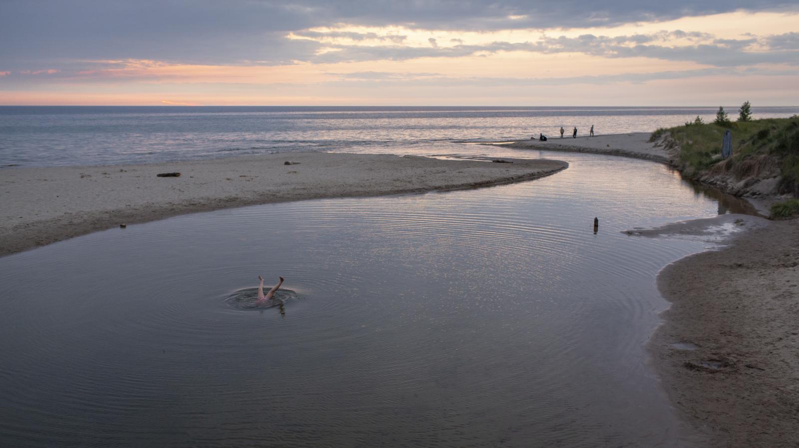 Portfolio - The sun sets over Lake Michigan as a swimmer flips upside...