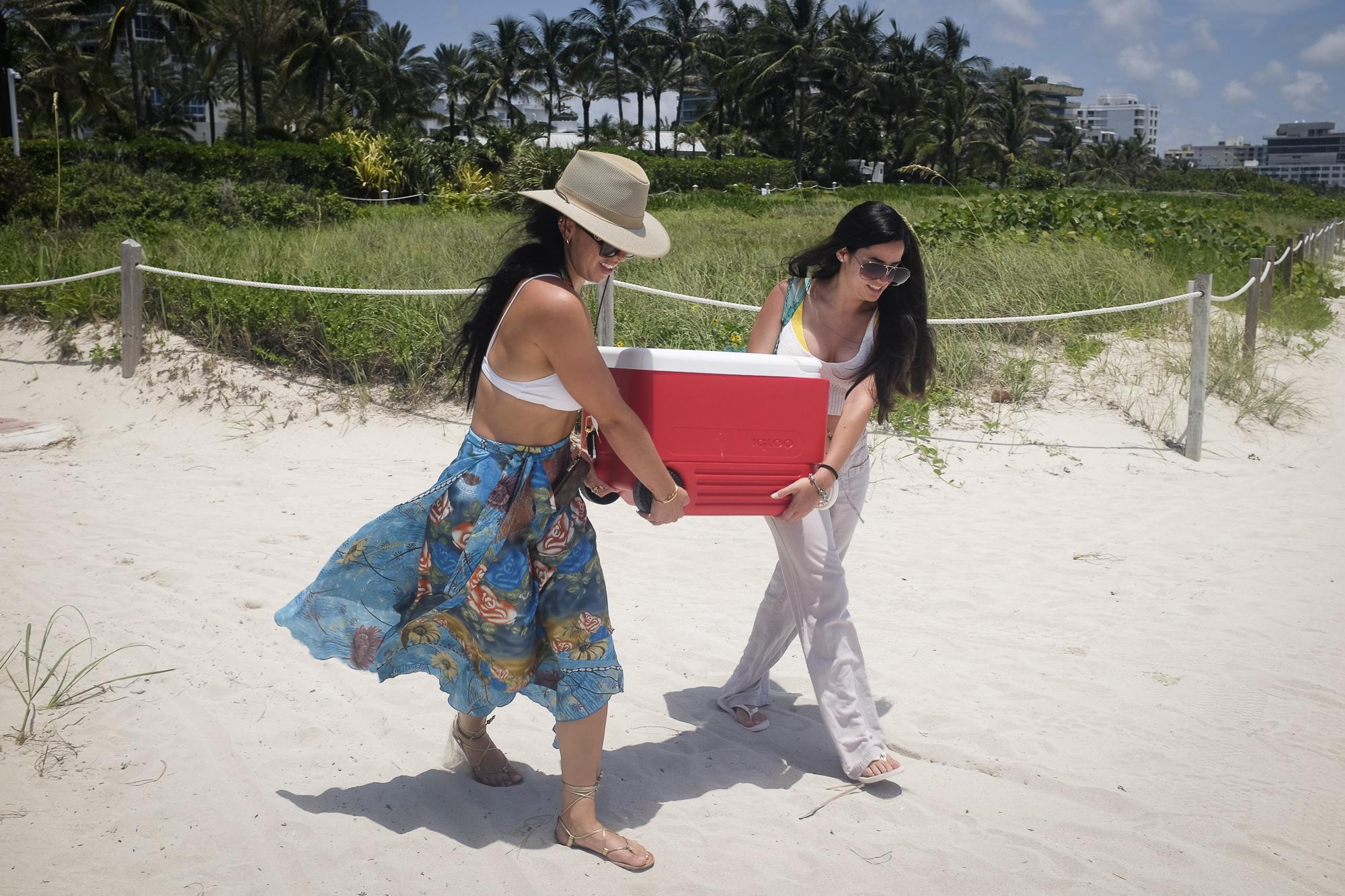 Beaches reopen with restrictions to limit the spread of the coronavirus disease  - Women arrive to the beach while carrying a cooler as...