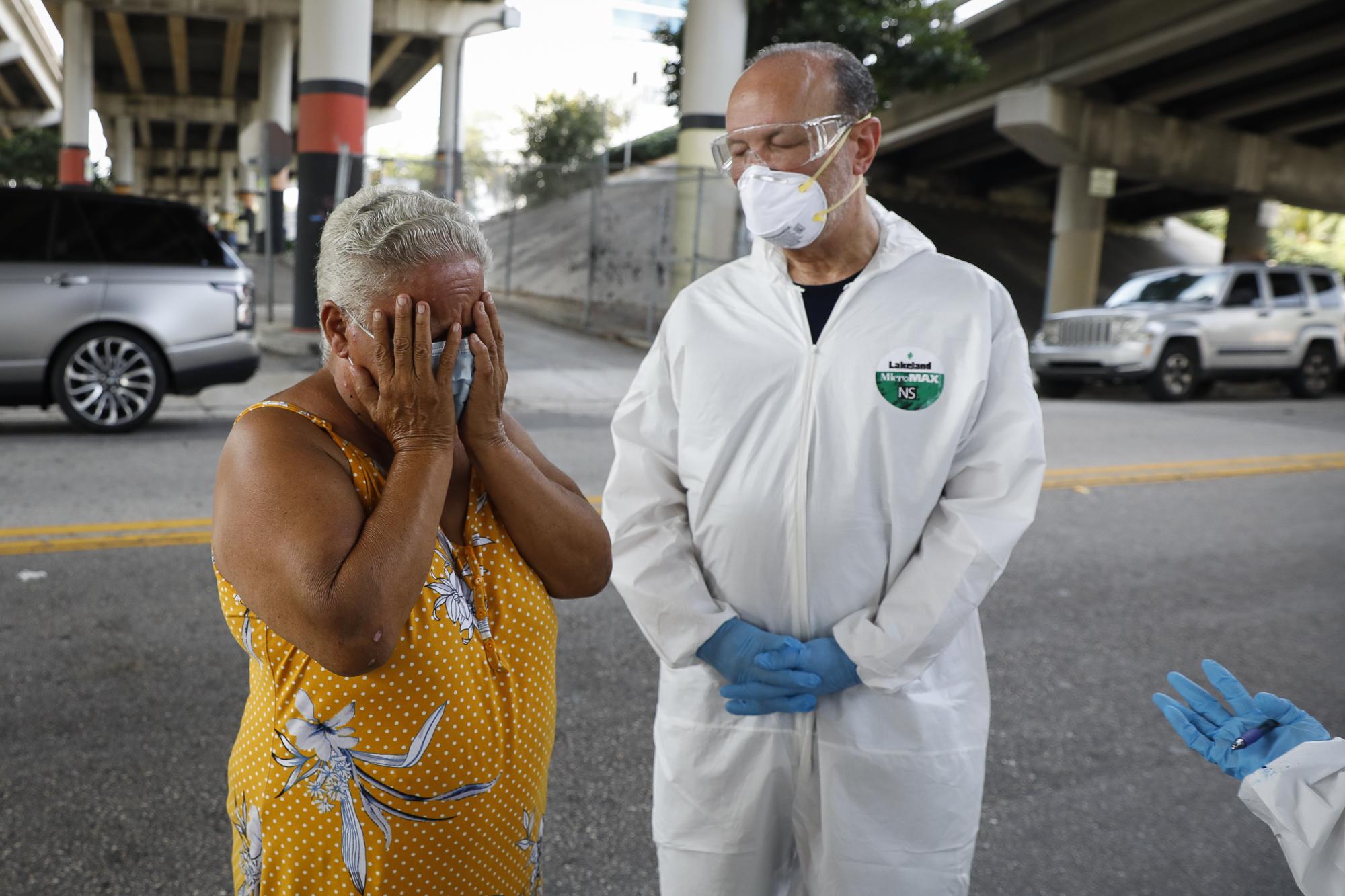 Miami-Dade County testing operation for the coronavirus disease - A homeless woman reacts next to a worker collecting...