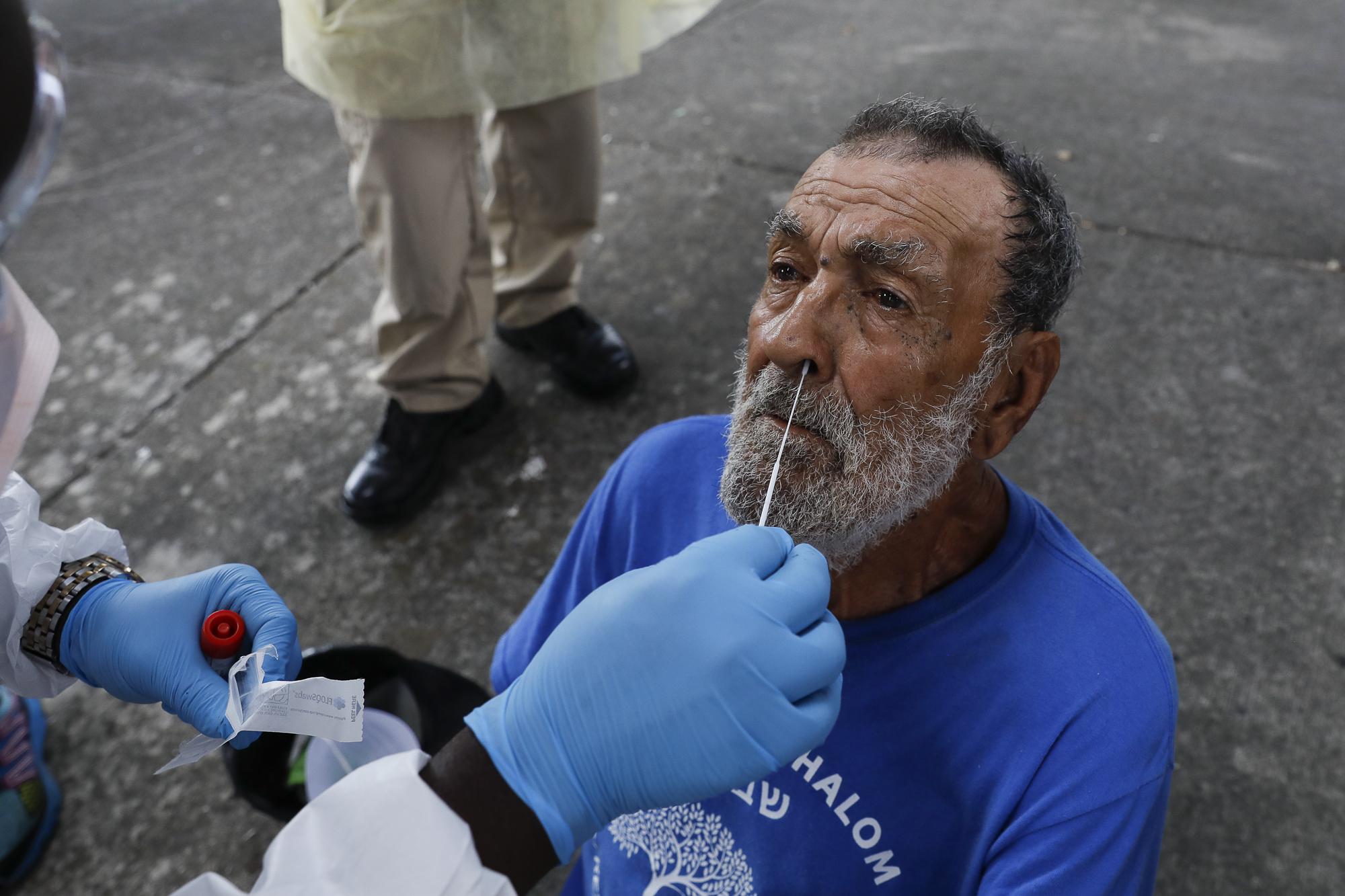 Miami-Dade County testing operation for the coronavirus disease - A homeless man reacts as a worker uses a swab to collect...