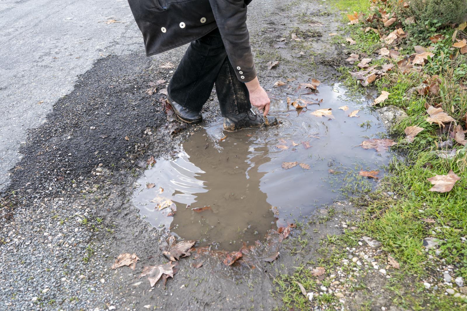   -  Ben gets rid of mud stuck on his boots using a small wooden stick and the water of a puddle, in...