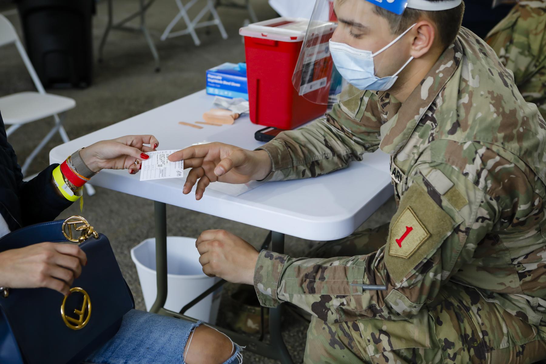 FEMA vaccination facility in North Miami - A U.S. Army soldier hands out a vaccine card in a...