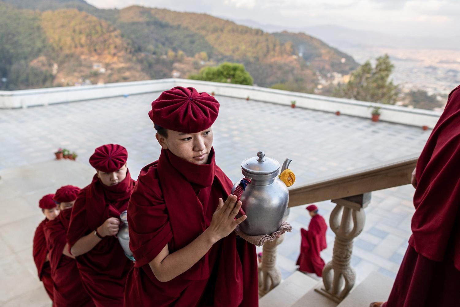 THE KUNG FU NUNS OF THE HIMALAYAS  - Young nuns arrive with tea pots during the evening puja...