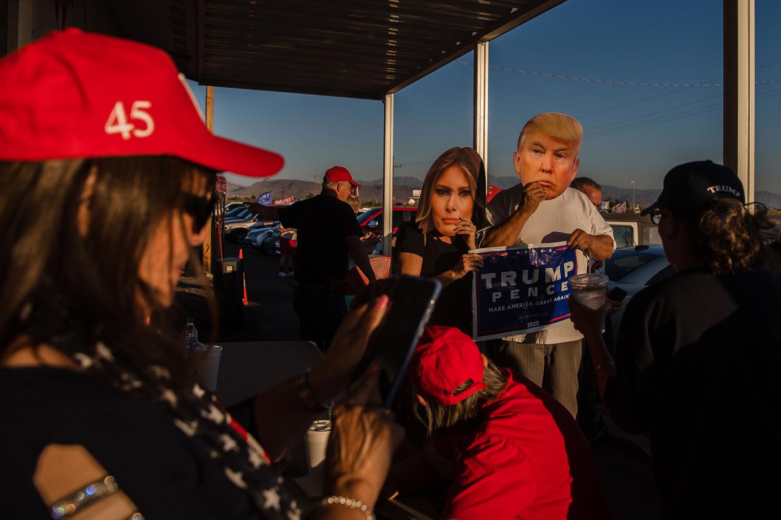 A man and woman wearing a President Trump and Melania Trump face masks get ready to pose for a photo in front of the Great American Pizza and Subs restaurant in Golden Valley, Arizona on October 22, 2020. Trump supporters gathered outside the restaurant to watch Biden and Trump&#39;s final debate.