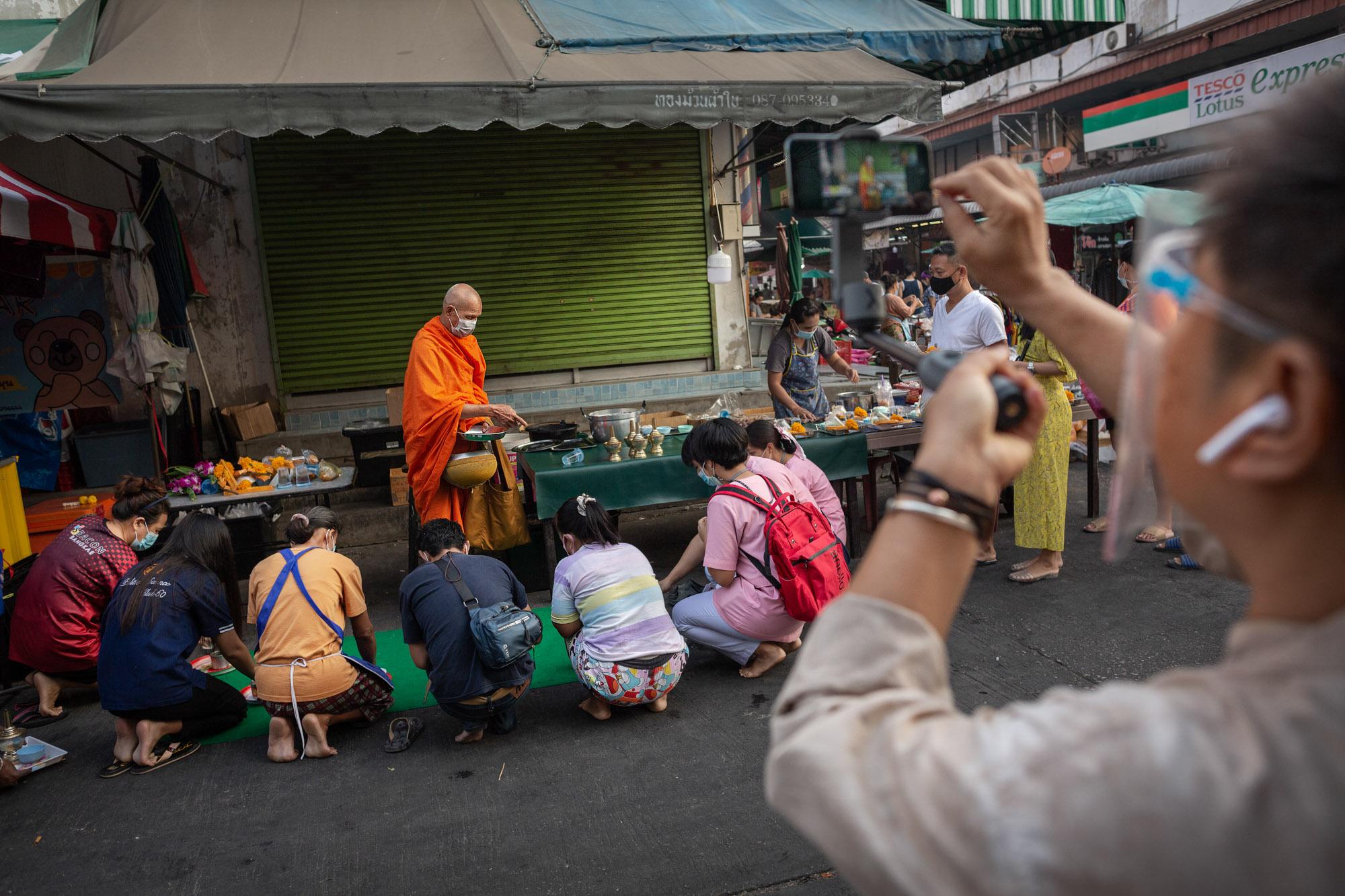 Hnoi Latthitham, 53, shows participants of a virtual tour an example of alms offering to a Buddhist monk at Chai Chimplee Temple Market in Bangkok,...