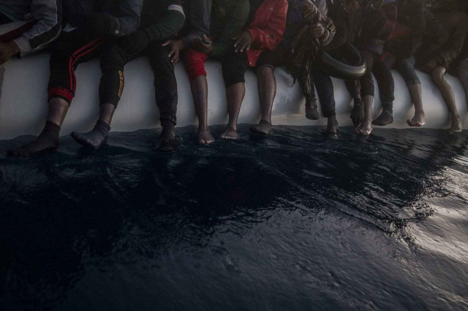 Fleeing the Libyan Clutches - Migrants and refugees are seen barefoot in a rubber boat....