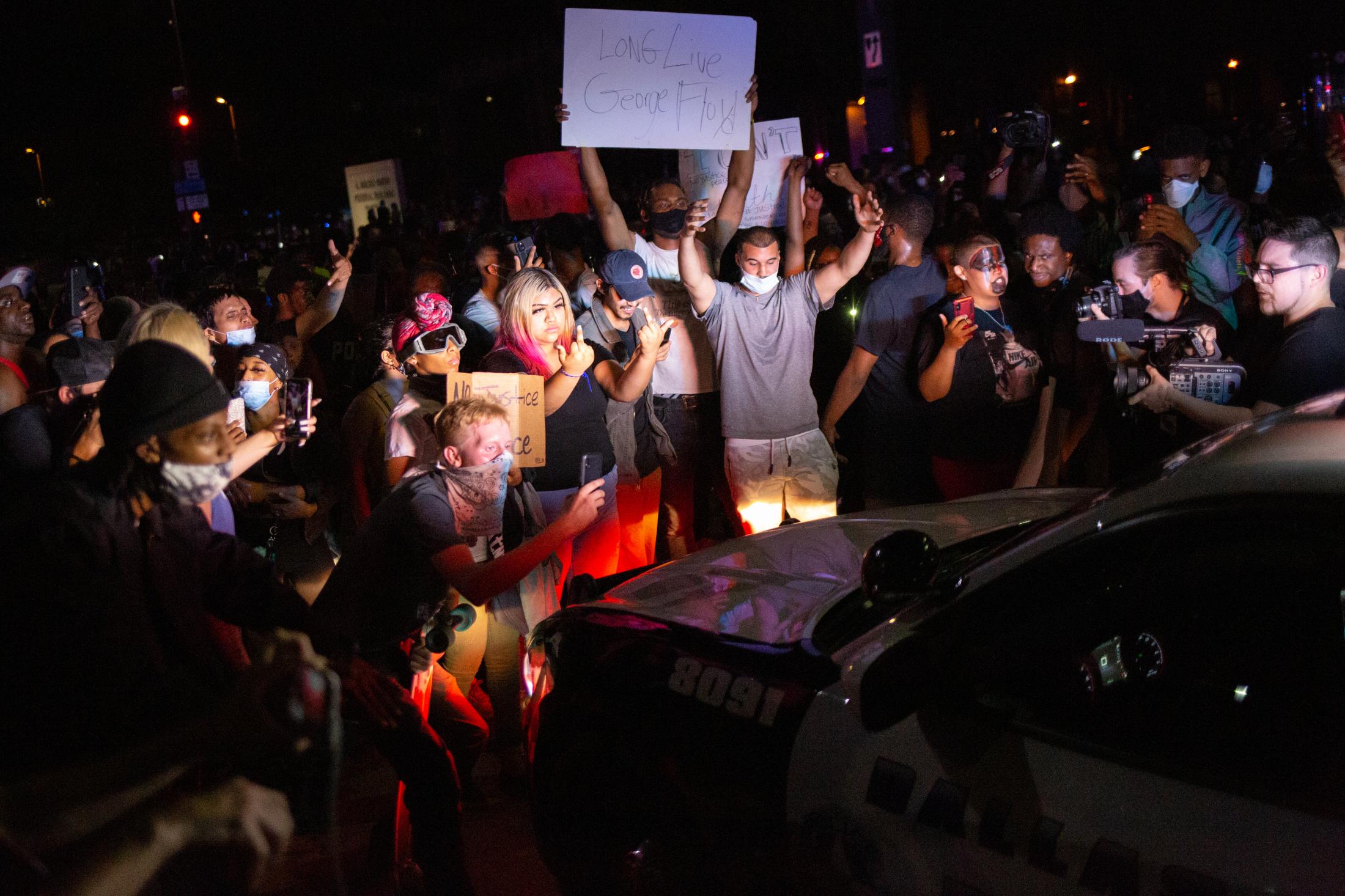Unrest Dallas - A crowd storms around a police cruiser with signs and...