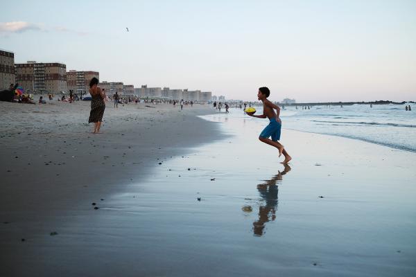 "New York is Back"? - Kid playing with football at sunset at Rockaway beach. July 2020, Queens.