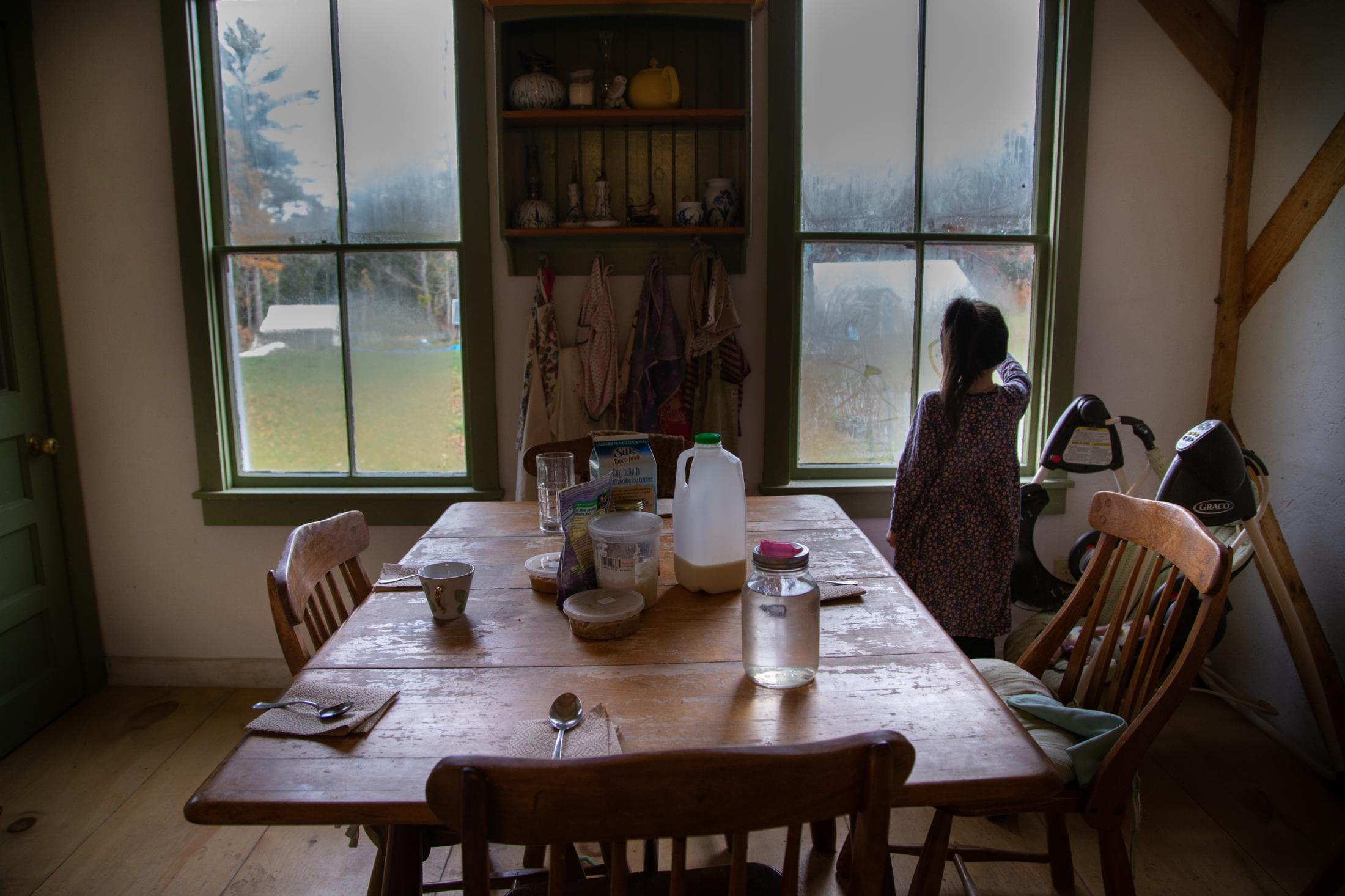 Lydia awaits for her breakfast while she draws on her home window, Bremen, Maine, 2014.
