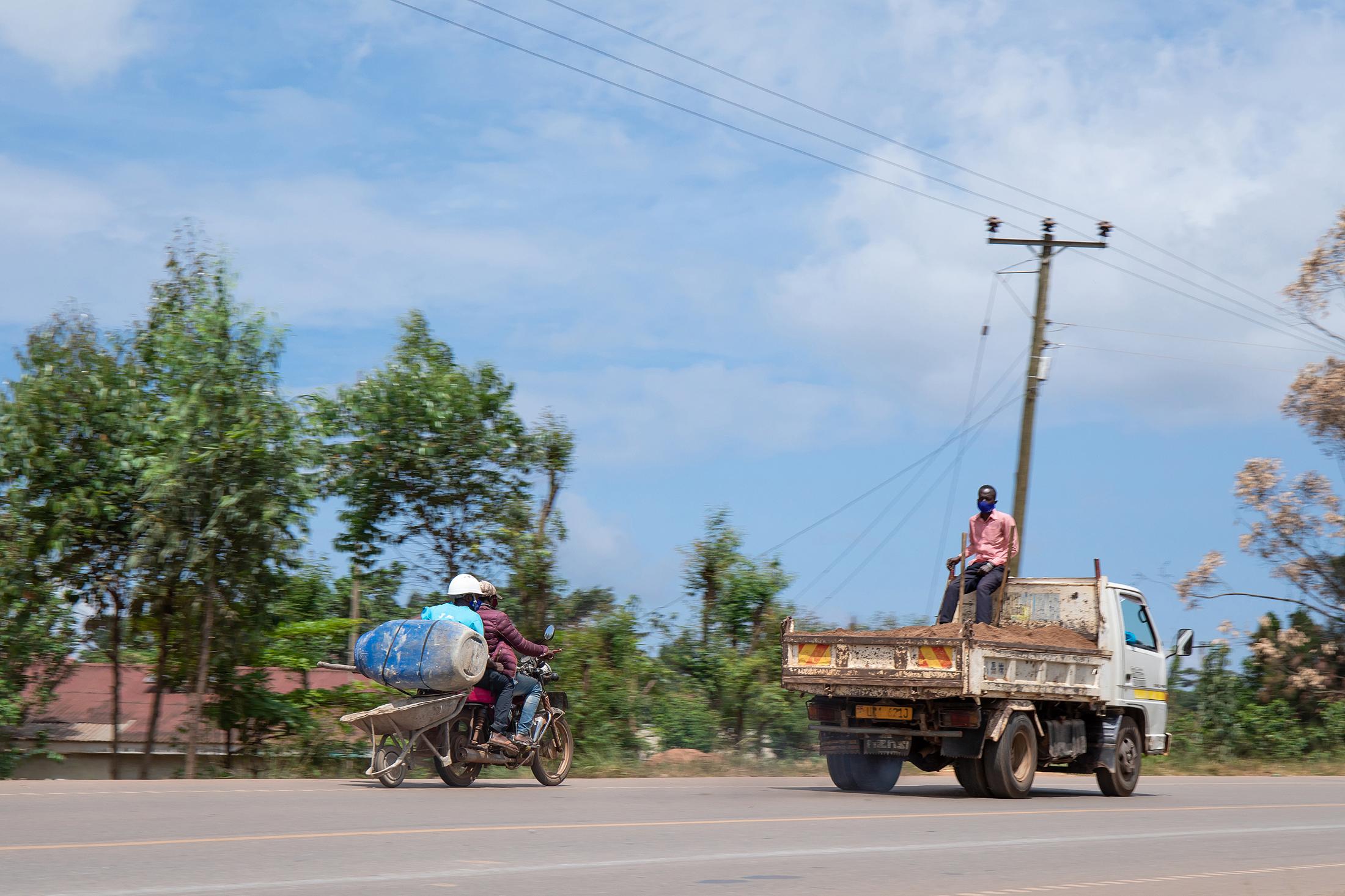 Domestic Express - Two builders on a motorbike with luggage and a wheelbarrow tied to the bike along Katosi road on...