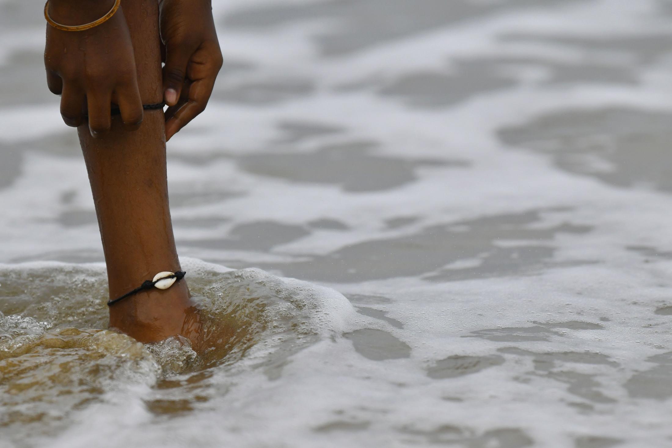 Kamali pulls up her trouser to show her anklet. Every surfer has a shell either around their ankle or neck. This is a sign of respect to the sea. Some also believe that this helps ward off evil eyes.