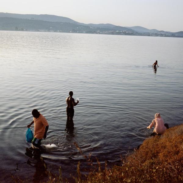 Image from In the Name of God -   Refugees swimming and showering in the sea inside the...