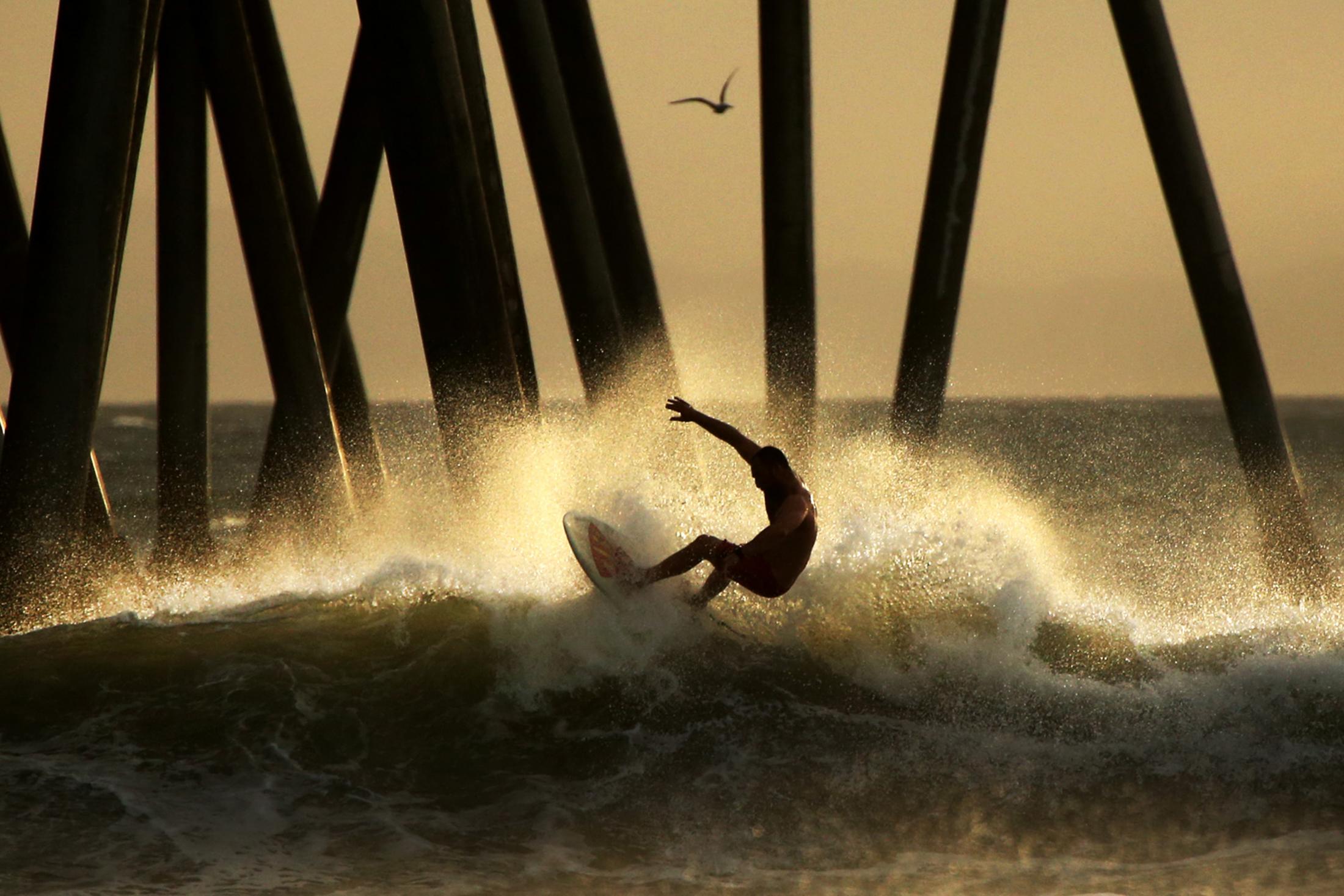 HUNTINGTON BEACH, CA - JANUARY 19: A surfer rides a wave near the Huntington Beach Pier on January 19, 2021 in Huntington Beach, California. A...