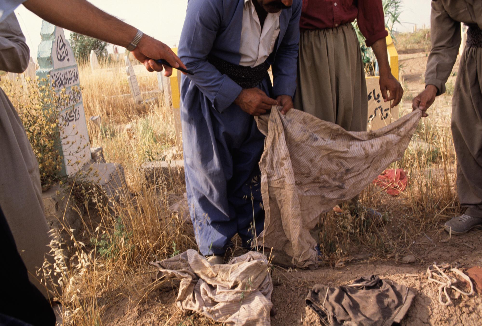 Kurdish men look closely at clothes left on top of graves marking unidentified bones exhumed...