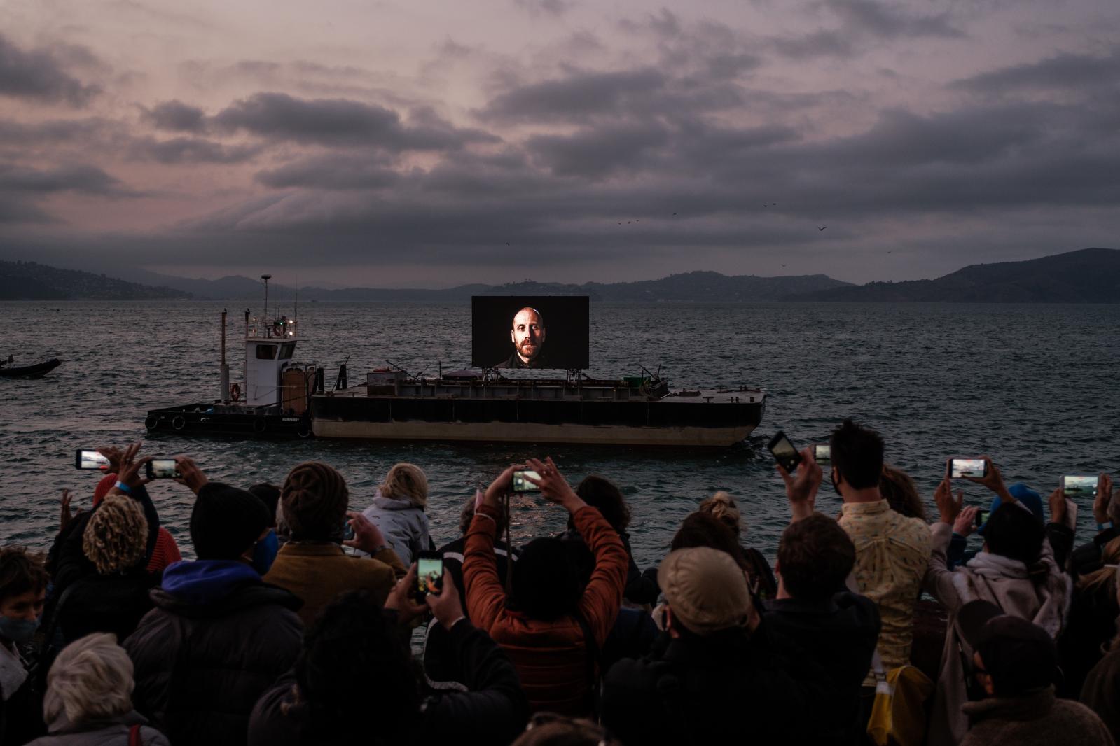 People gather at Fort Mason to view &ldquo;Night Watch&rdquo; a floating media installation created by Shimon Attie that displays portraits of refugees granted asylum in the U.S, in San Francisco on Friday, September 17, 2021.