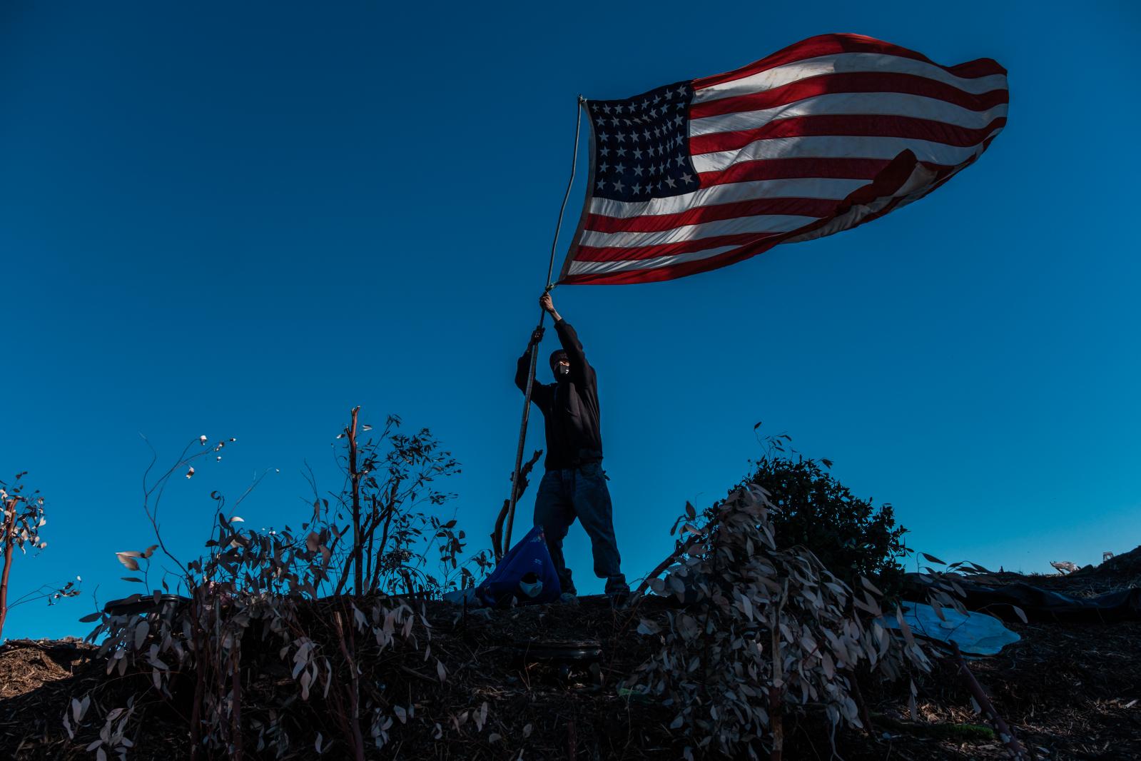 A man identified as Junior adjusts his American flag at the RV encampment where he lives on Thanksgiving day in San Francisco on Thursday, November 26, 2020.