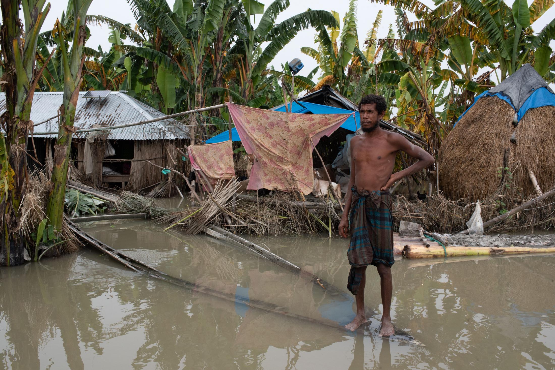 The Depth of Flood - A flood-affected man stands in the water on a boat as his...