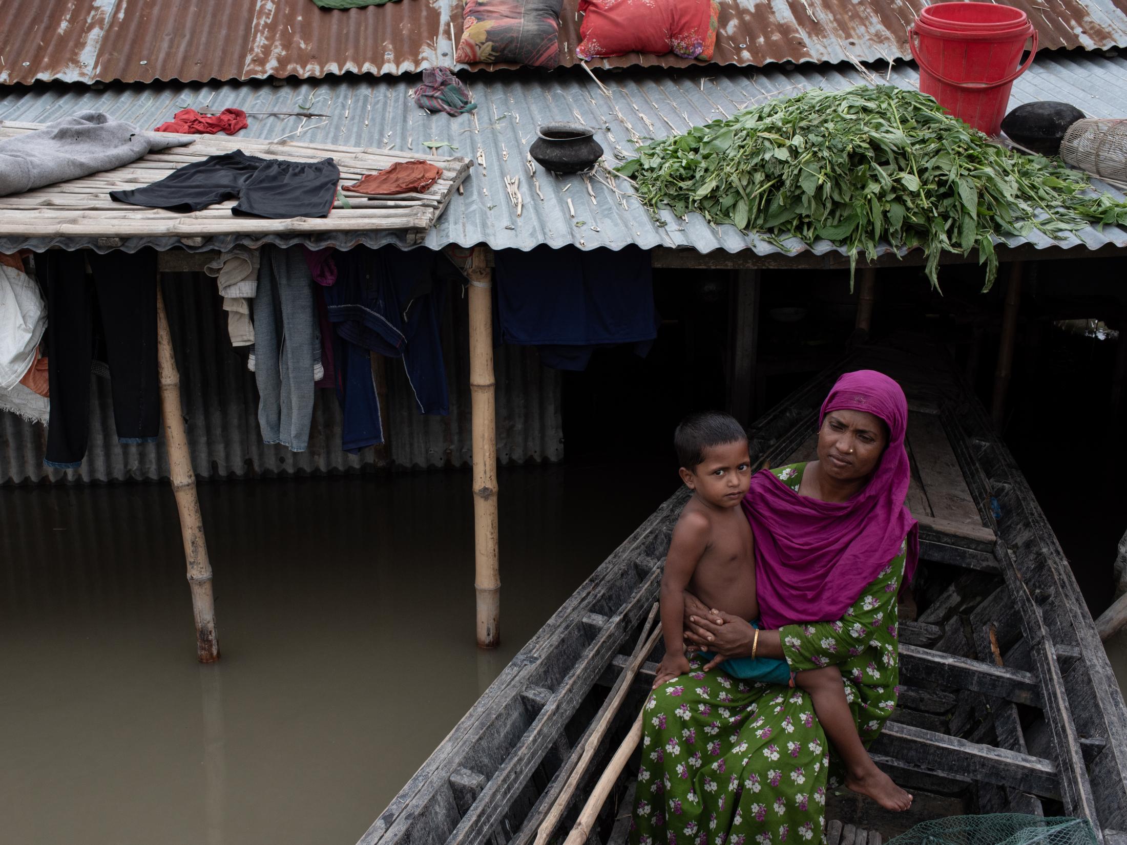 The Depth of Flood - A woman with her baby girl sits on a boat as his house...