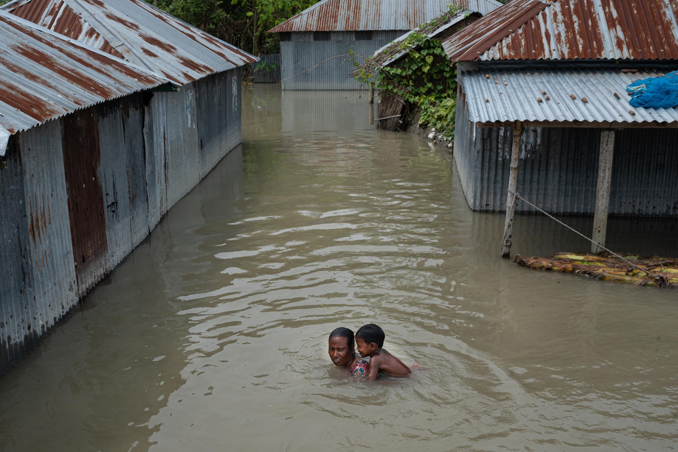 The Depth of Flood - A woman with her baby girl on her back swims through...