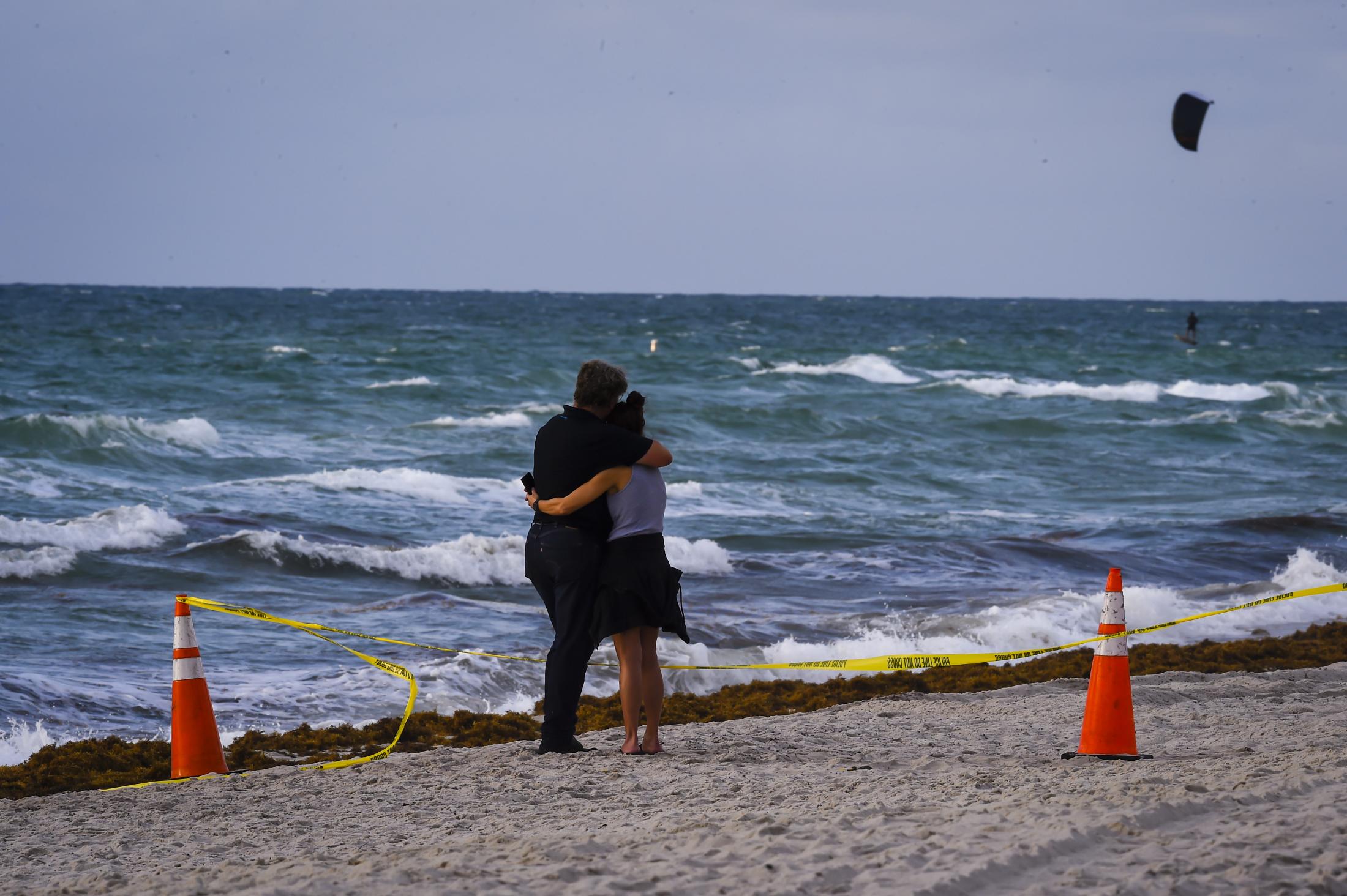 2021 - Surfside building collapsed - A couple hugs next to a partially collapsed building in...