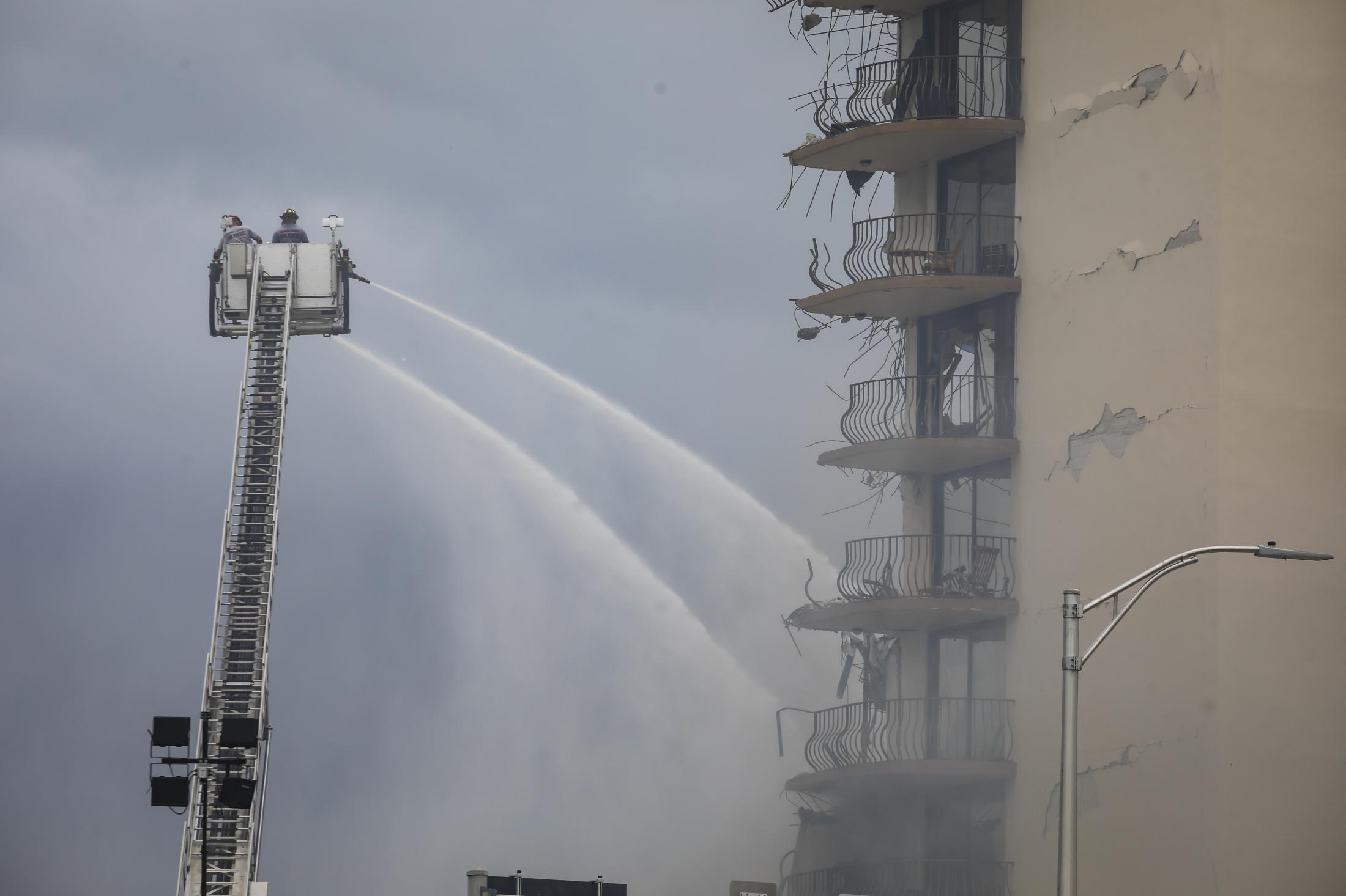 2021 - Surfside building collapsed - Rescue workers on a crane spray water to the debris of a...