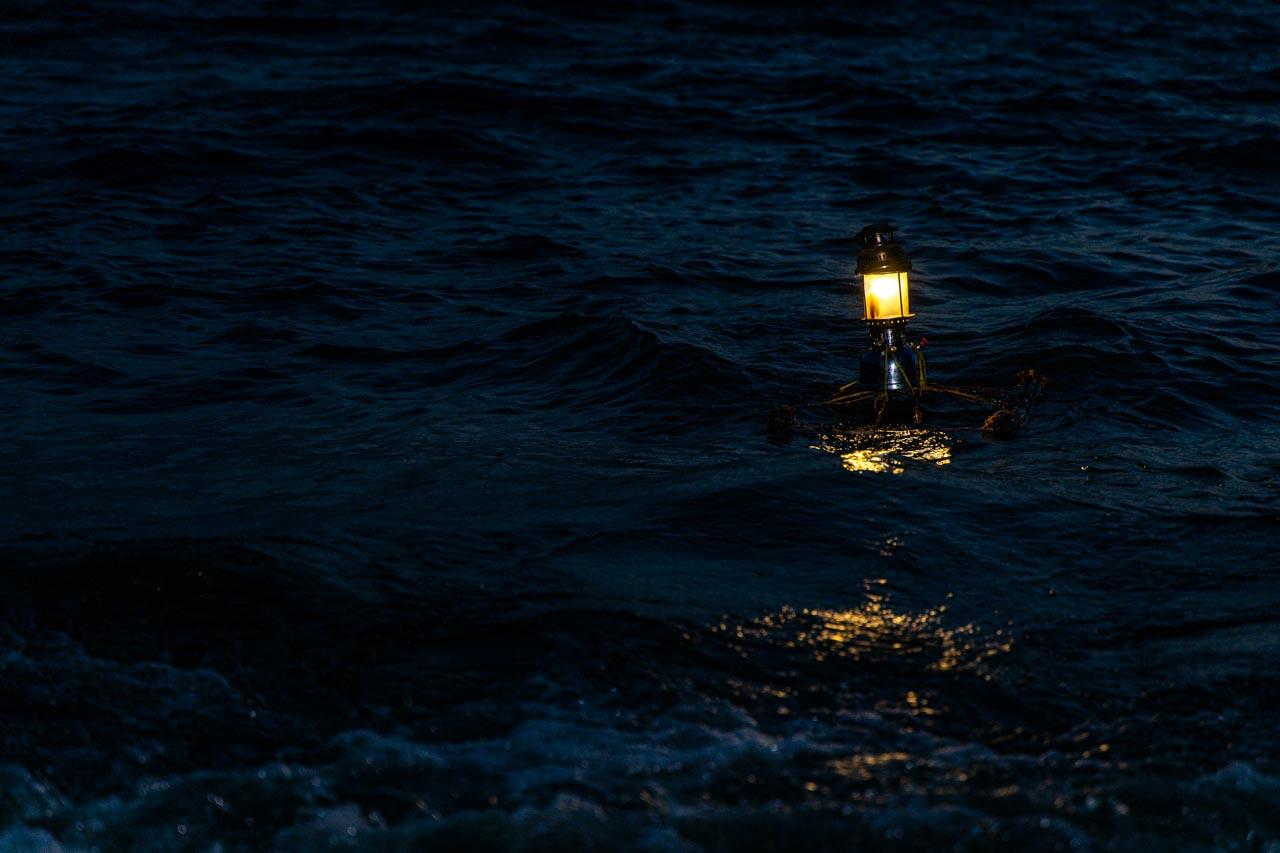 A kerosene lamp floating on the fishing stand, Lake Victoria. The lamp produces yellow light from burnt kerosene, which is derived from petroleum, a fossil fuel. When the fishermen relied on kerosene, the light would last only for a few hours, and they had to check and refill the lamps when they were in the water. Now, the solar lamps can last the whole night.