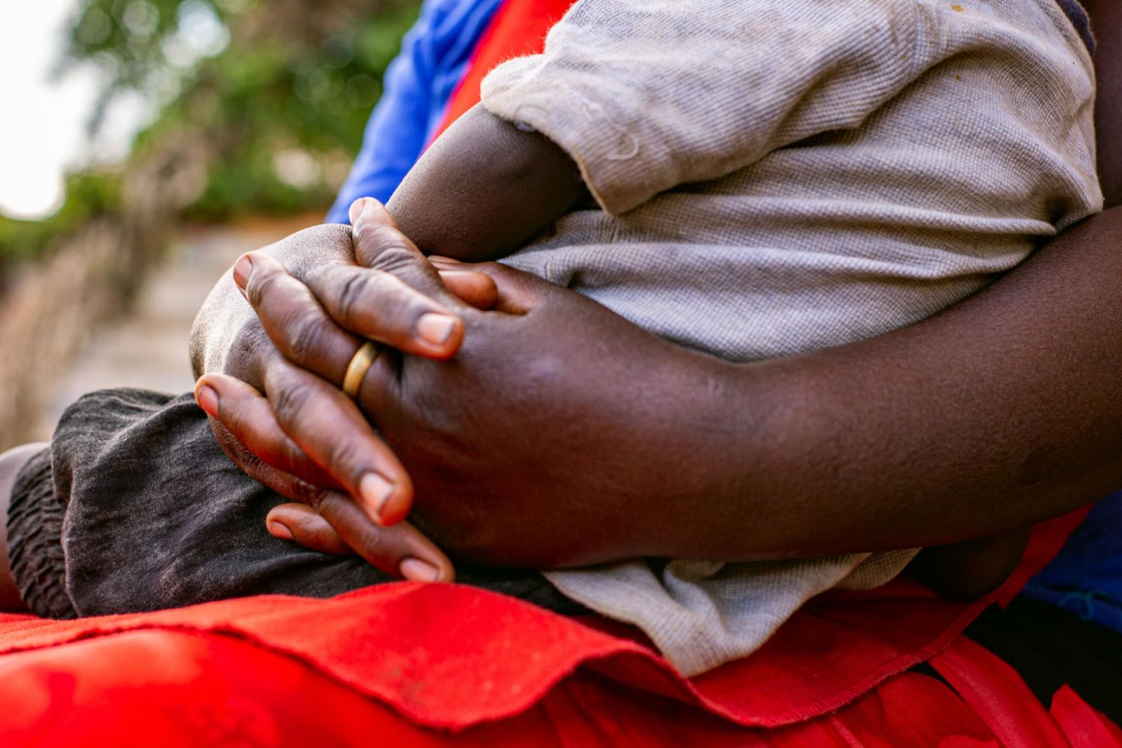 A mother of 18 sits with her son in her arms. The ring she wears is a symbol of marriage, and thus society&rsquo;s acceptance of teenage parenting and marriage. 