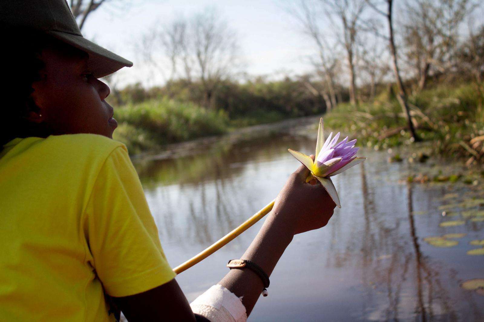 Edith, a snake handler working with Uganda Reptile Village, looks out across a wetland while holding a water lily.