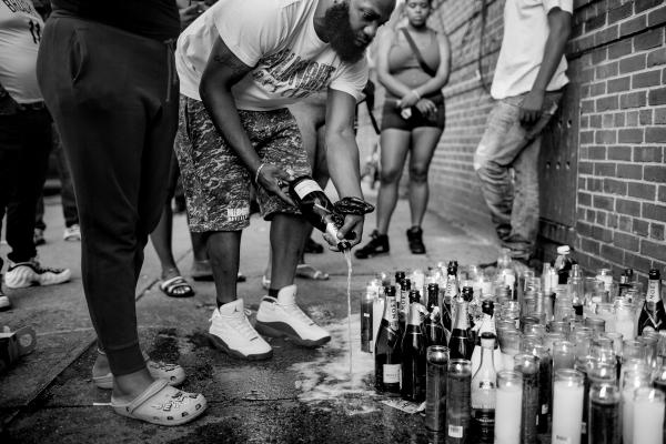 Image from United We Thrive-Divided We Die - Community members pour champagne on the sidewalk to honor...