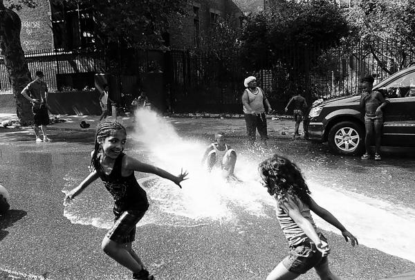Children playing with a water hose during a hot spring day, in Crown Heights.