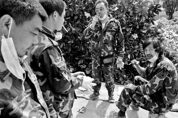 China Quake Aftermath - Residents taking a smoke break, while salvaging their...