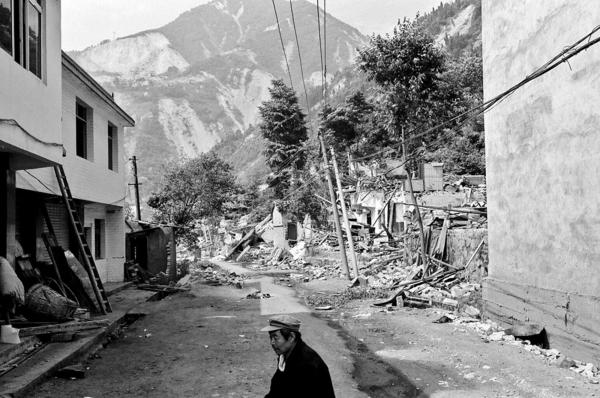 A quake survivor sitting outside his destroyed home and shop, waiting for soldiers to come and help him clear rubble from his house. Yingxiu town, Sichuan province.