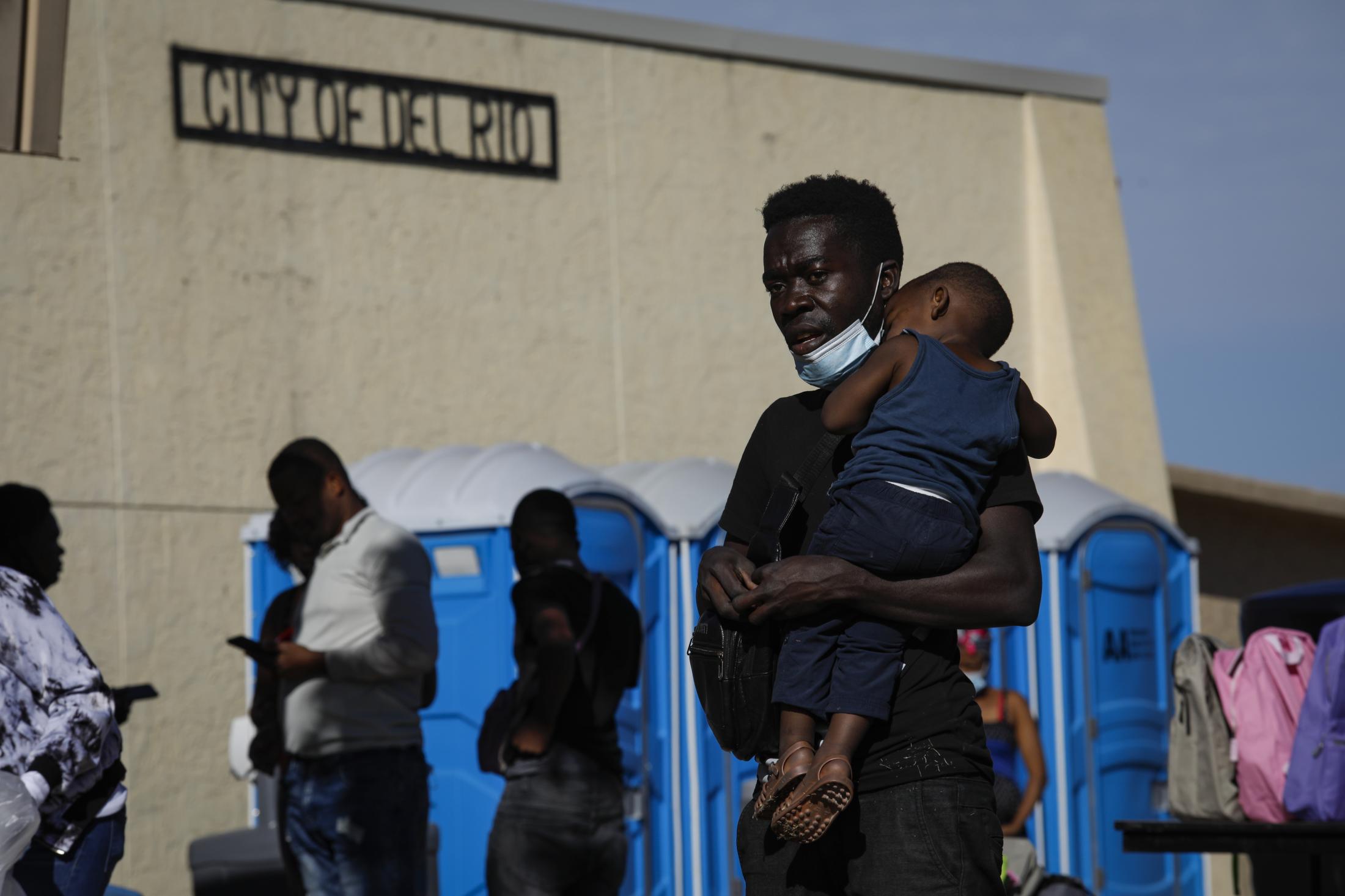 U.S. removes asylum-seeking migrants from Texas border camp - A man carries a child as he waits in line with others...