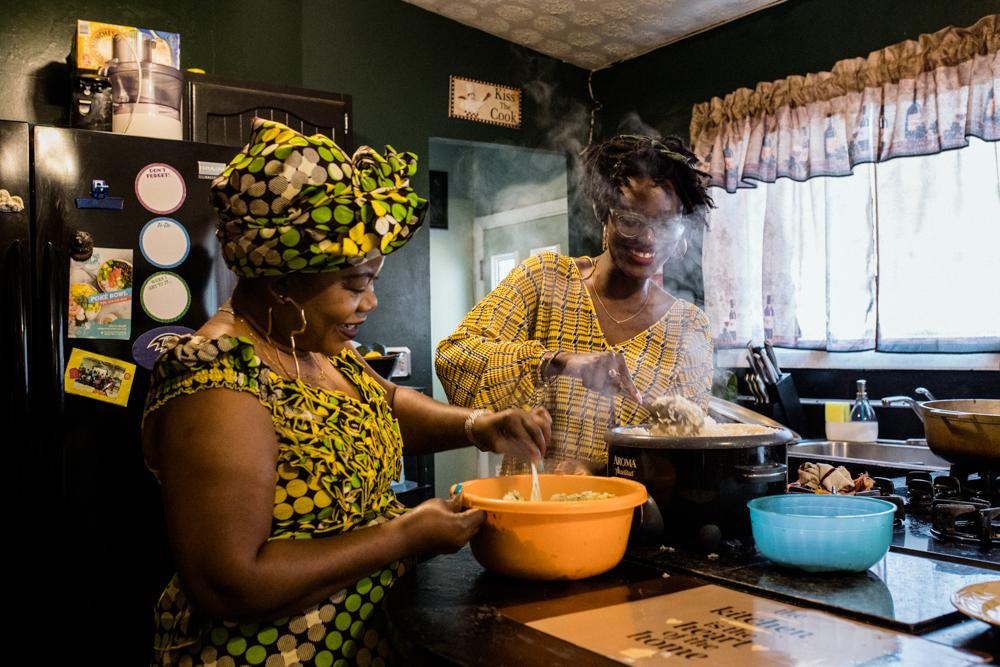 PIKESVILLE, MD - OCTOBER 28, 2021: Bilphena Yahwon, 28, helps her mother Tryphena Teah, 49, make chuck rice by combining Jute leaves with cooked rice in Pikesville, Maryland on October 28, 2021. Chuck rice and gravy are some of the commonly made dishes for Liberian Thanksgiving. (Photo by Rosem Morton for The New York Times)
