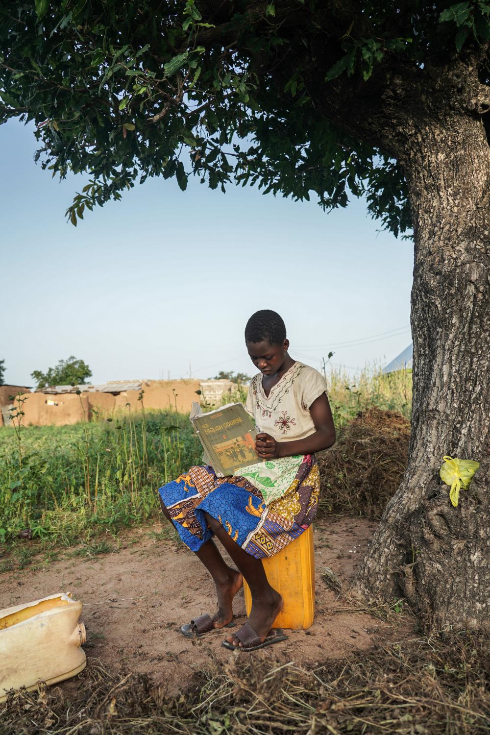 Tales Under the Baobab Tree - Florence Azudaa (13) reads after school outside her...