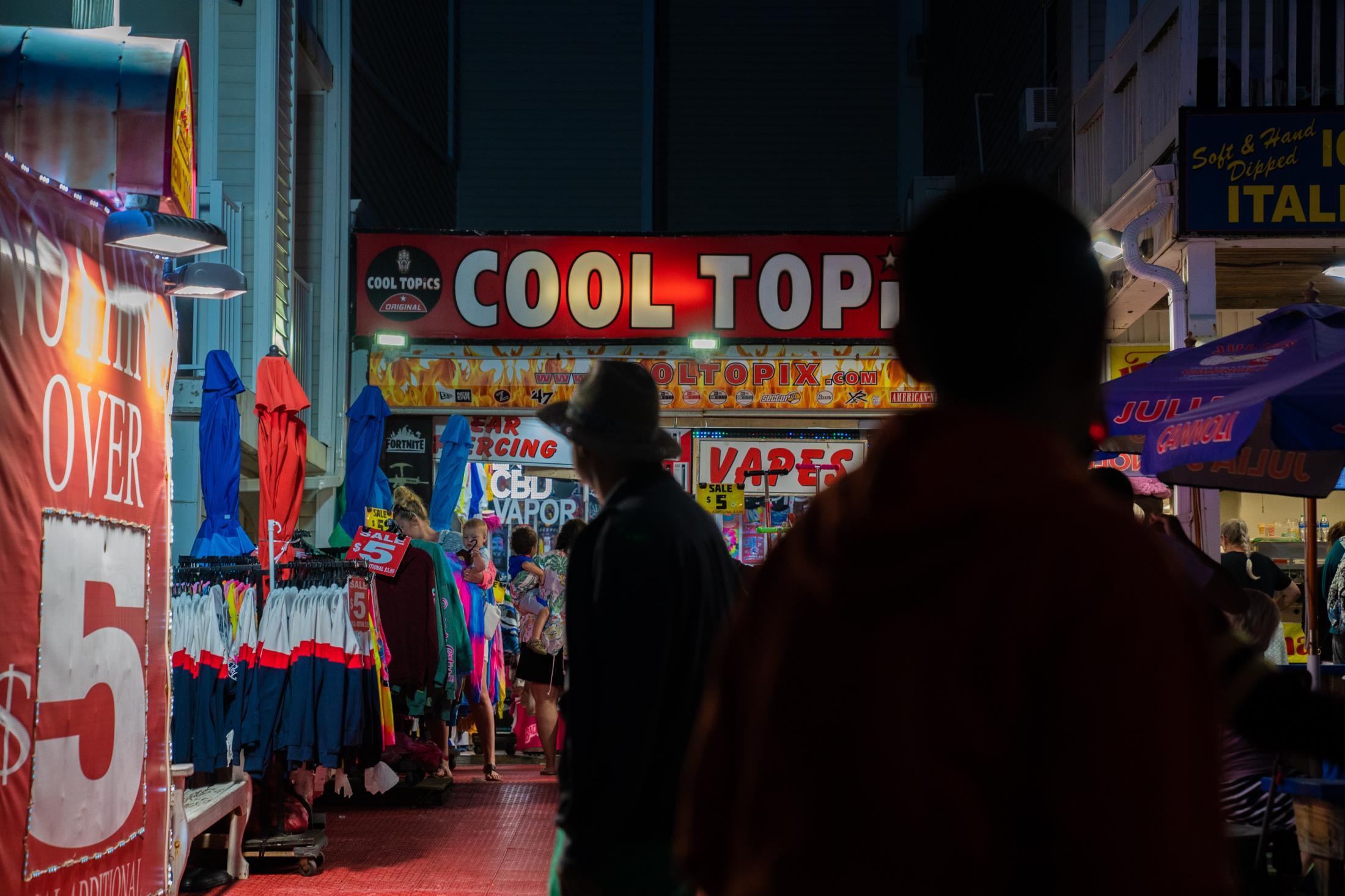 People walk by a vape shop at night on the Boardwalk in Ocean City, MD on June 16, 2021.