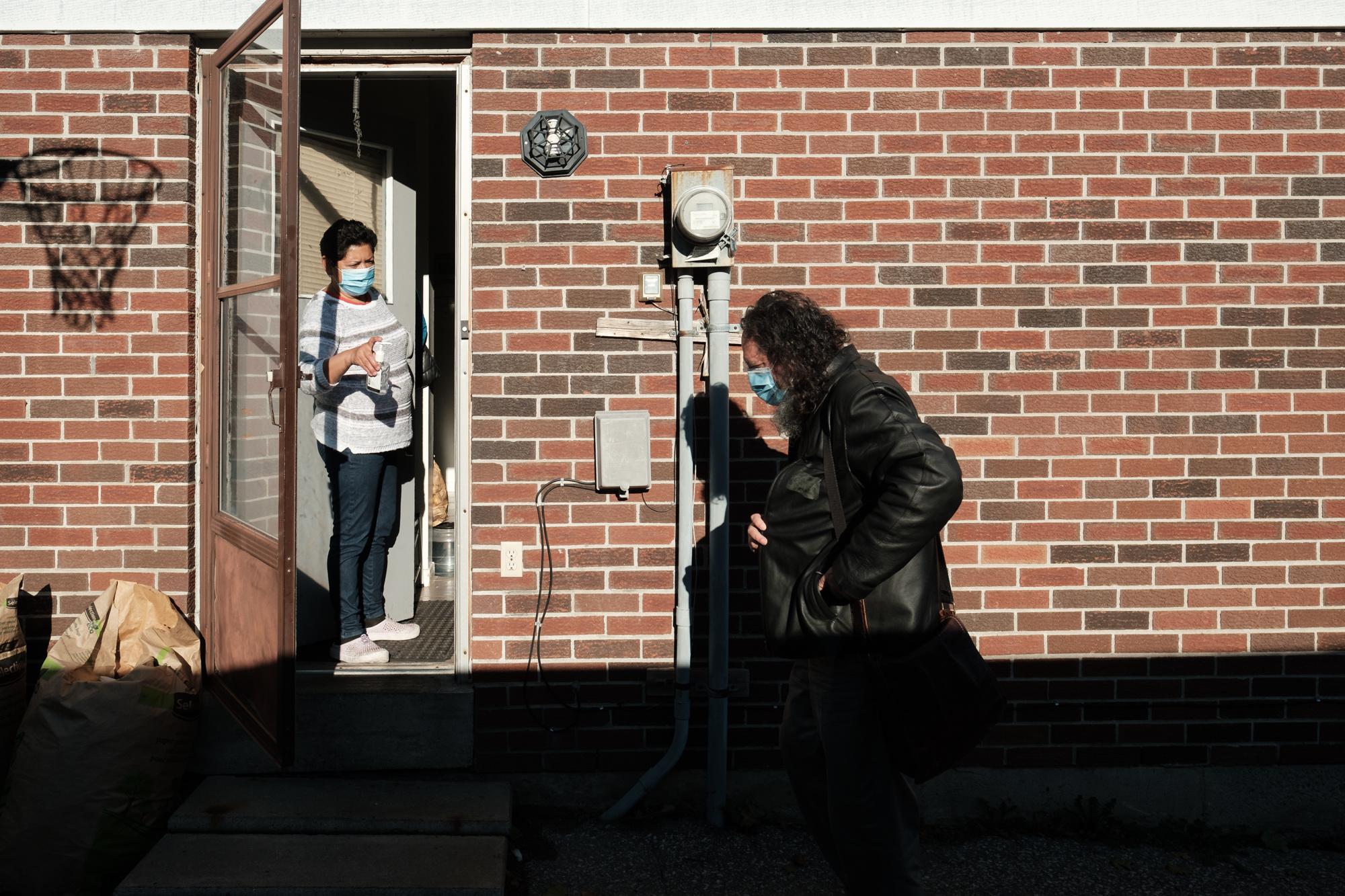 Carmen Rosa greets Astudillo at her door with a bottle of hand sanitizer. November, 2020. Carmen Rosa recibe a Astudillo en su puerta con una...