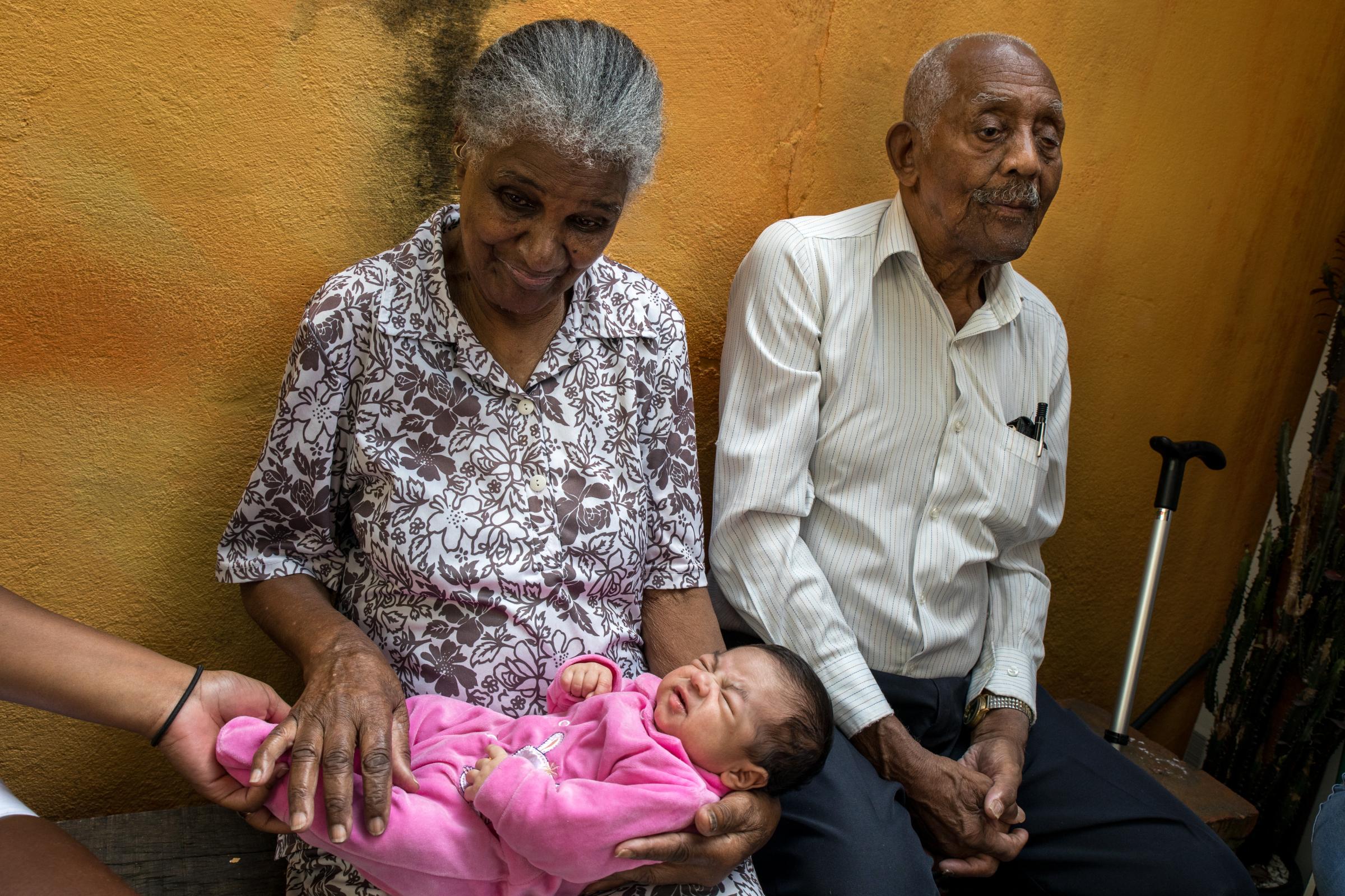 &nbsp;In Sao Paulo, Brazil, Gerald da Silva Balbino (92) sits beside his wife, Paula (90), as she holds their great-granddaughter. Brazil once...