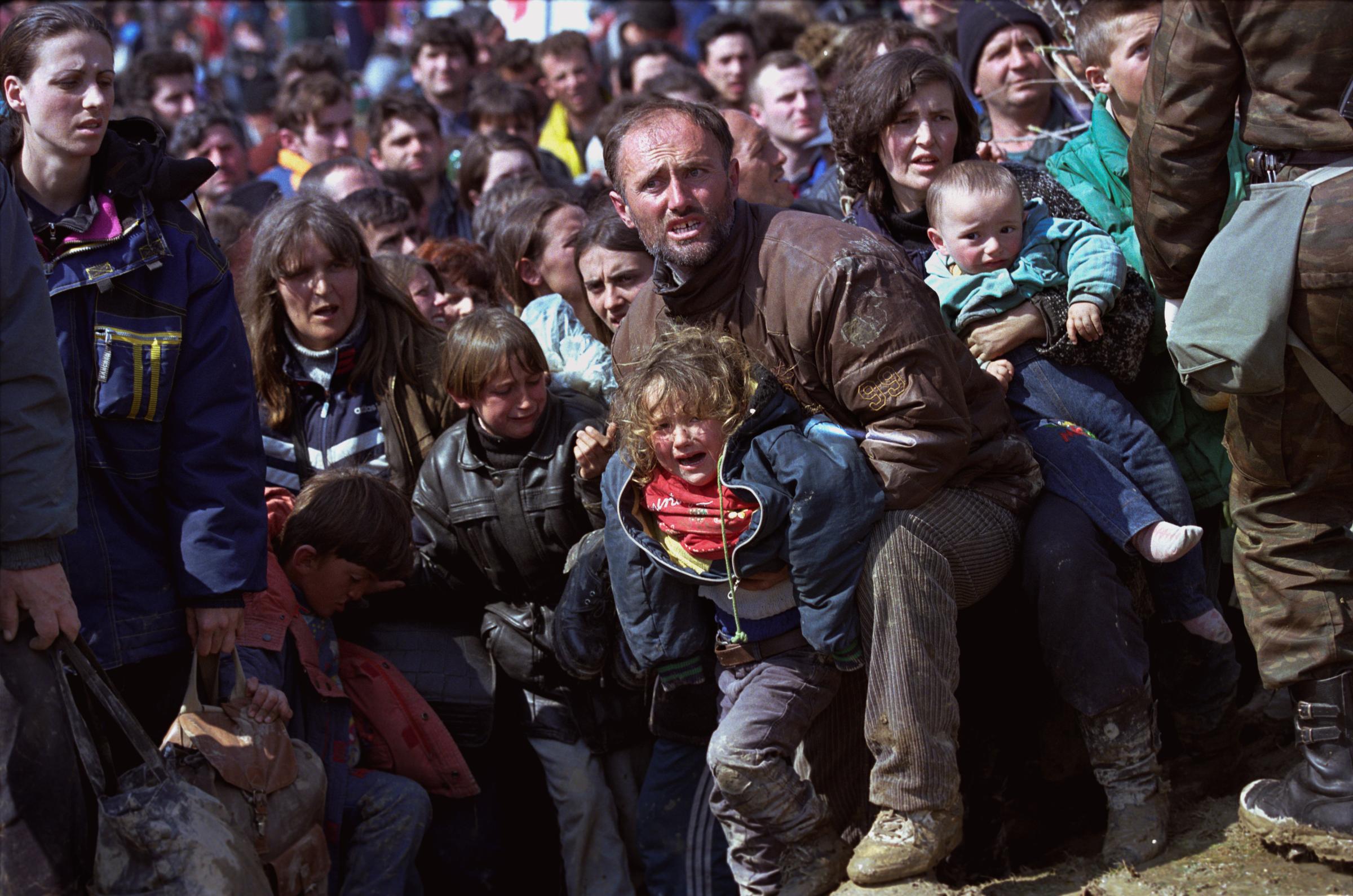A father pleads with Macedonian soldiers to allow his sick child into a medical tent on the Macedonian side of the border.