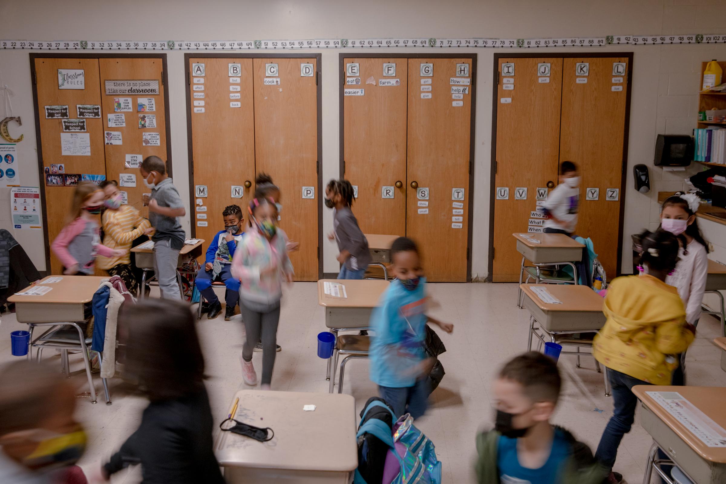 Singles - Students run between desks with a mask on during a...