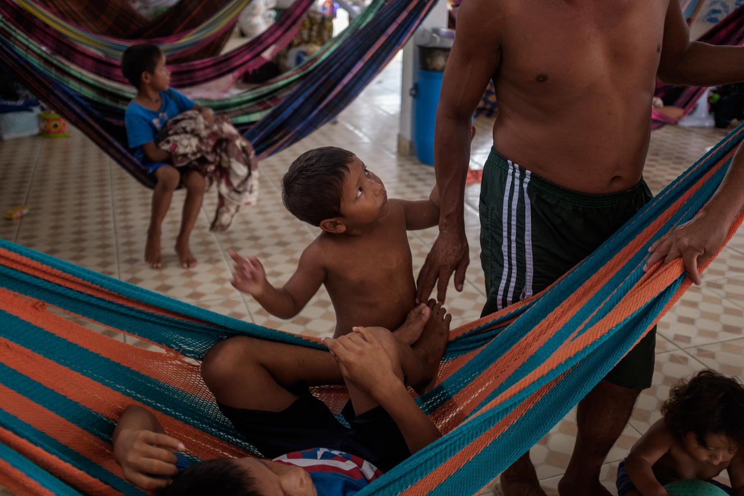 A Warao child tries to get his father&#39;s attention at a makeshift shelter housing Venezuelan indigenous refugees in Manaus in Amazonas state, Brazil, November, 2020. Indigenous people have been migrating to the city from all over the region for decades, looking for work, access to education, jobs and healthcare and a better life. Like the refugees form Venezuela, many indigenous people arrive in the city to find a shortage of housing, poor access to public services, discrimination and a faltering economy aggravated by a deadly pandemic.