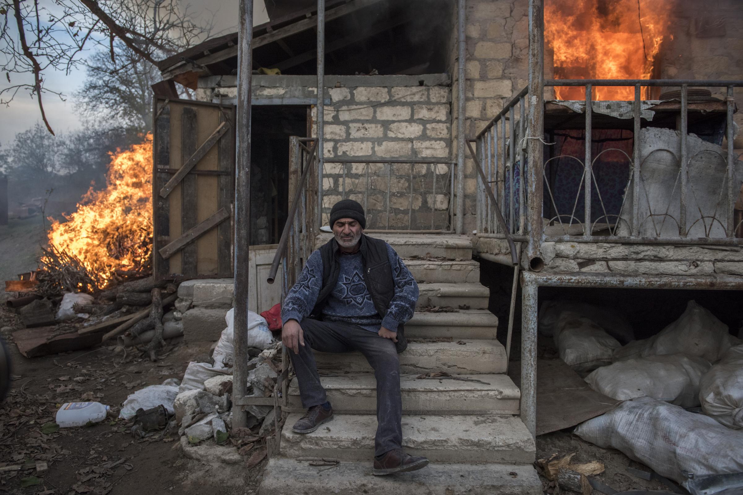 Paradise Lost - A local resident of Areg sits outside a burning house in the village of Karegakh,...