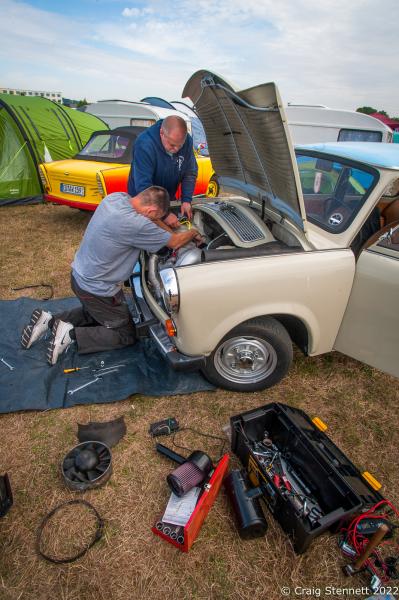 ZWICKAU, GERMANY- SEPTEMBER 01: Maintenance work under way on a &#39;Trabi&#39; at the Trabant Club Zwickau annual gathering of Trabi owners in 2018. The engine for the 500, 600 and the original 601 was a small two-stroke engine with two cylinders, accounting for the vehicle&#39;s modest performance. Its curb weight was about 600 kilograms (1,323 lb). When it ceased production in 1989, the Trabant delivered 19 kilowatts (25 hp) from a 600 cc (37 cu in) displacement. It took 21 seconds to accelerate from zero to its top speed of 100 km/h (62 mph). The engine produced a very smoky exhaust and was a significant source of air pollution: nine times the hydrocarbons and five times the carbon-monoxide emissions of the average 2007 European car. Its fuel consumption was 7 l/100 km (40 mpg‑imp; 34 mpg‑US). Since the engine did not have an oil pump, two-stroke oil had to be added to the 24-liter (6.3 U.S. gal; 5.3 imp gal) fuel tank[13] at a 50:1 (or 33:1) ratio of fuel to oil at each fill-up. Contemporary gas stations in countries where two-stroke engines were common sold a premixed gas-oil mixture at the pump. Because the Trabant had no fuel pump, its fuel tank was above the motor so fuel could reach the carburetor by gravity; this increased the risk of fire in front-end accidents. Earlier models had no fuel gauge, and a dipstick was inserted into the tank to determine how much fuel remained. Best known for its dull color scheme and cramped, uncomfortable ride, the Trabant is an object of ridicule for many Germans and is regarded as symbolic of the fall of the Eastern Bloc. Known as a &quot;spark plug with a roof&quot; because of its small size, the car did gain public affection. Its design remained essentially unchanged from its introduction in the late 1950s, and the last model was introduced in 1964. In contrast, the West German Volkswagen Beetle received a number of updates (including improvements in efficiency) over a similar period. (Photo by Craig Stennett/Getty Images)